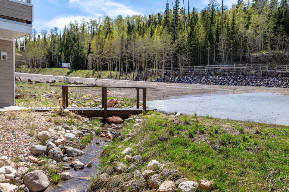 Wood bridge over a natural stream, with a gravel parking area and a forested backdrop