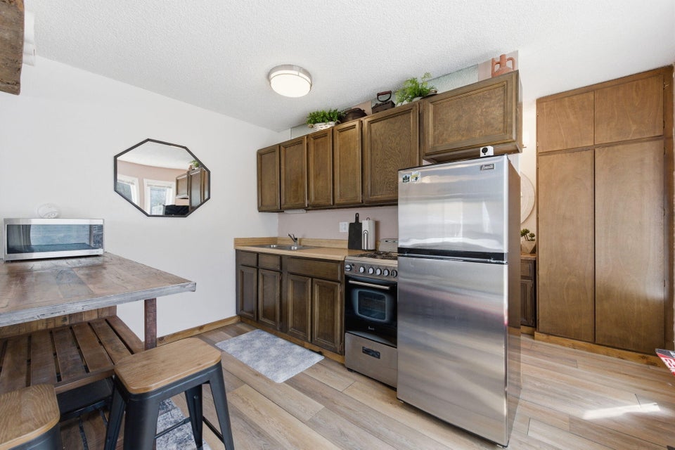 Compact kitchen featuring wood-finish flooring, dark wood cabinetry, and a full-size stainless steel refrigerator