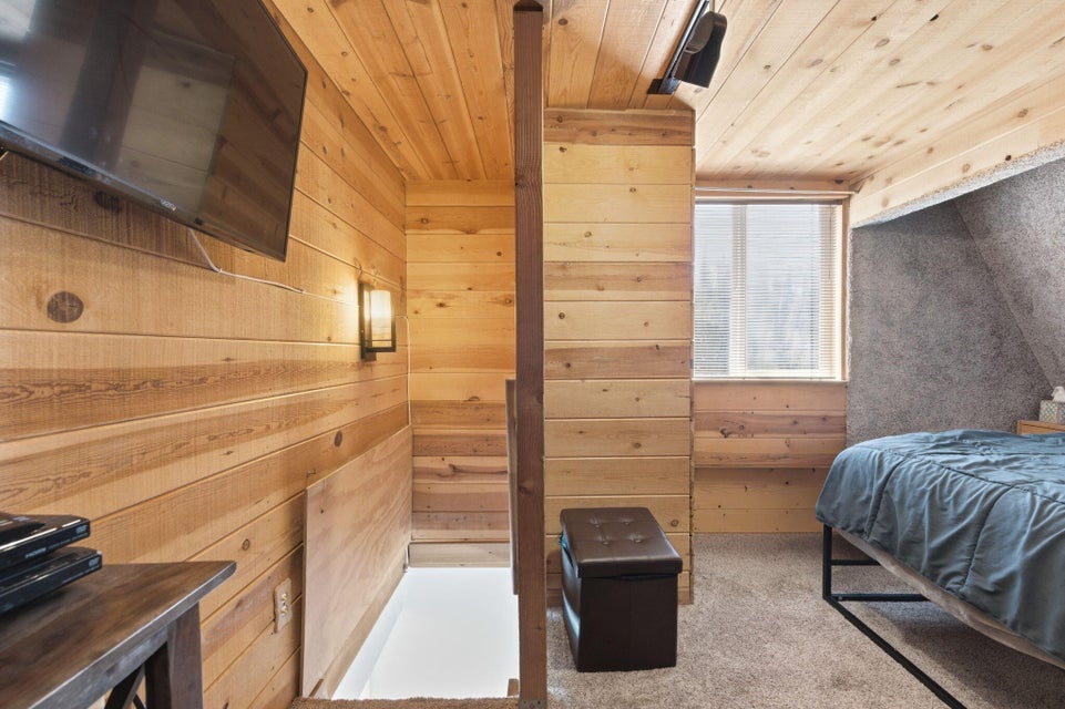 Wood-paneled room featuring a window with white blinds, wall-mounted television, and a built-in wall sconce
