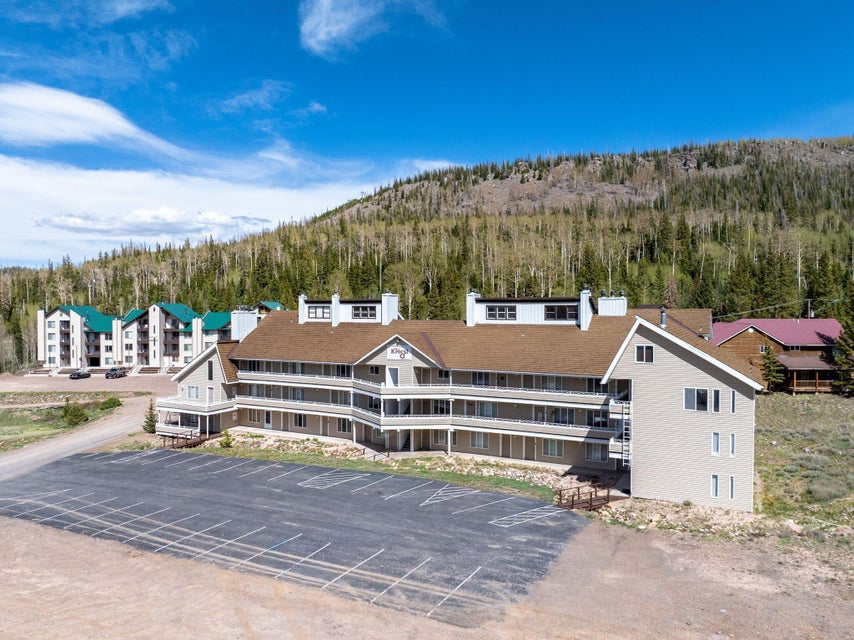 Multi-story building featuring a pitched shingle roof, multiple balconies, and a paved parking area