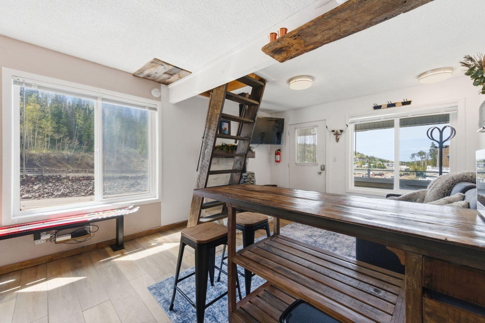 Open-concept living area featuring wood-finish flooring, a prominent wooden ladder, and exposed ceiling beams