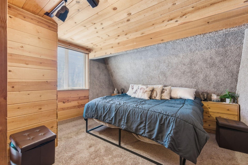 Bedroom featuring wood-paneled walls and ceiling, textured wall finish, and a window with blinds
