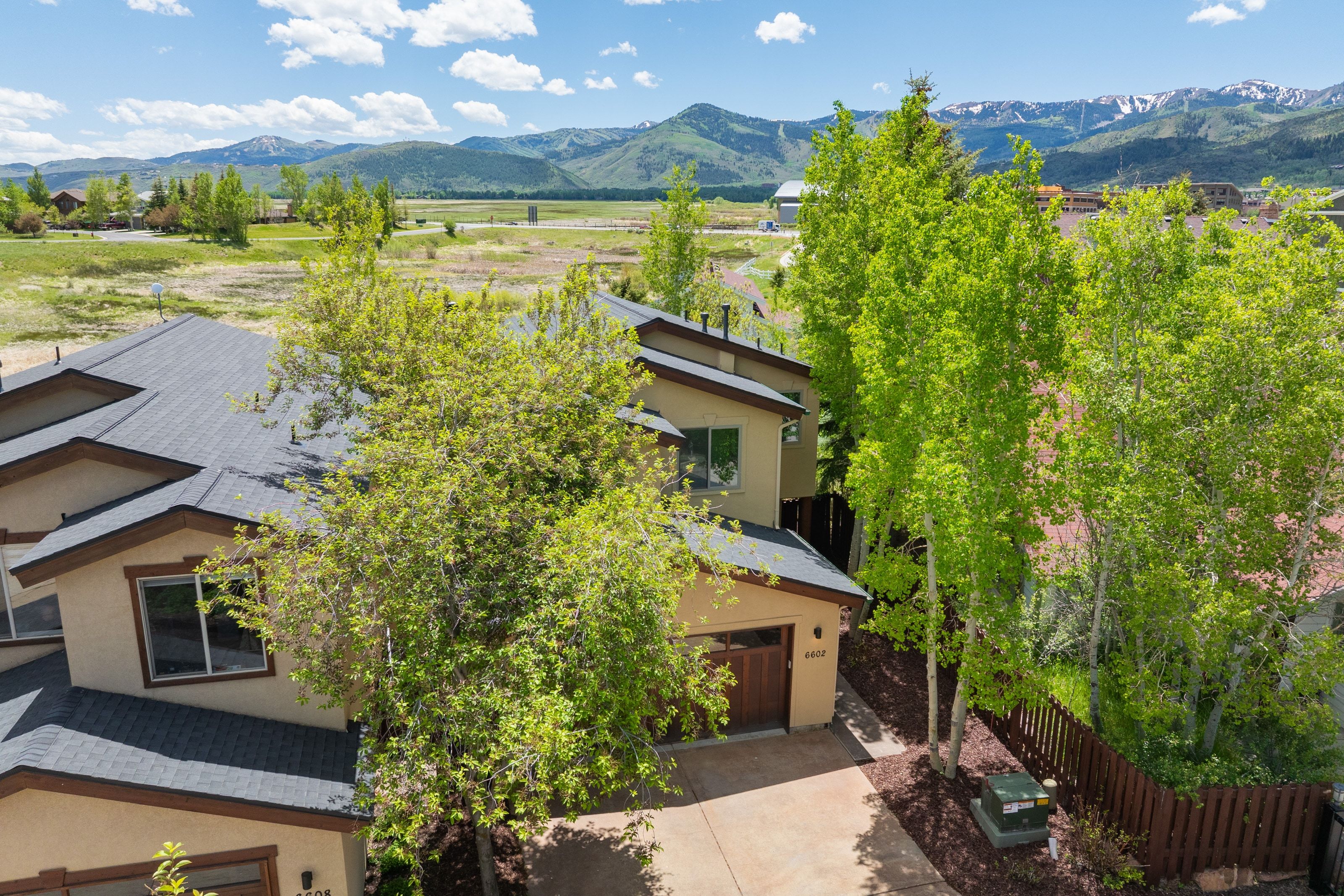 Contemporary stucco exterior featuring a dark asphalt shingle roof, brown trim, and a prominent wood-finish garage door