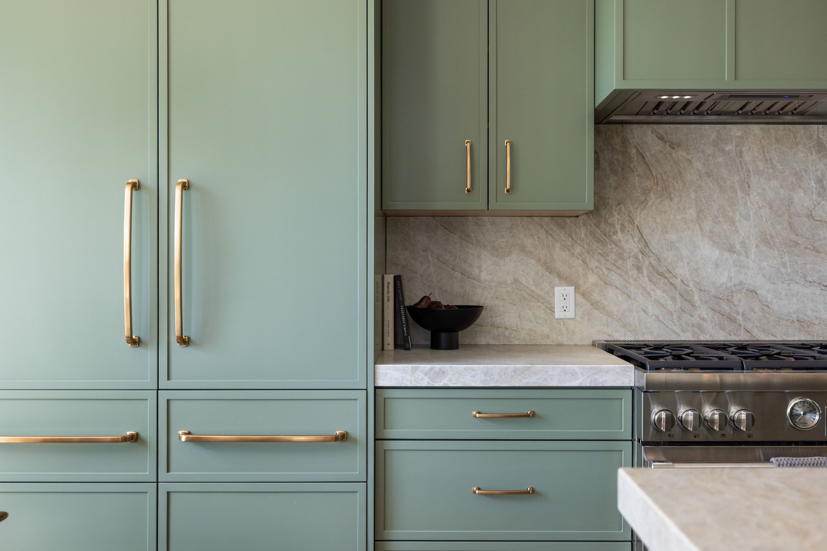 Custom panel-front refrigerator and cabinetry featuring a soft green finish and brass hardware