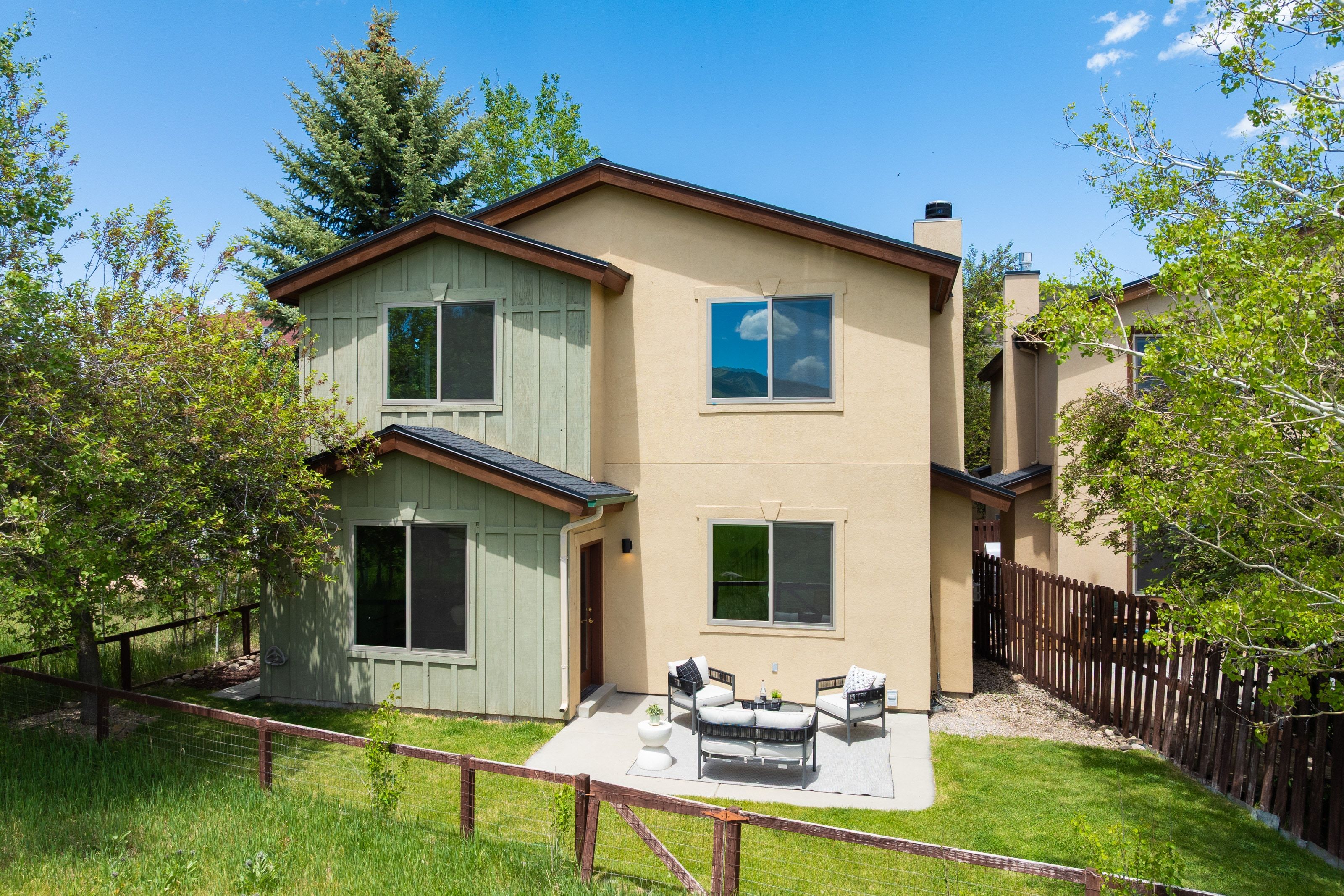 Two-story exterior featuring a stucco finish with board and batten accents, a concrete patio, and a fenced yard
