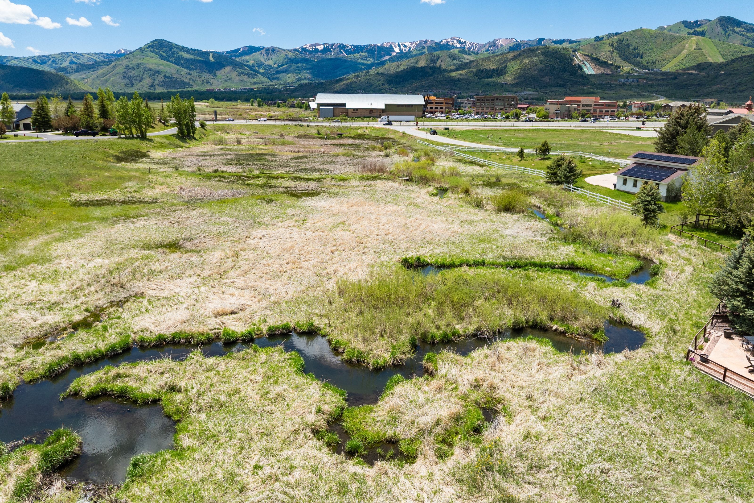 Expansive property featuring a winding stream, varied natural vegetation, and distant mountain ranges with snow-capped peaks