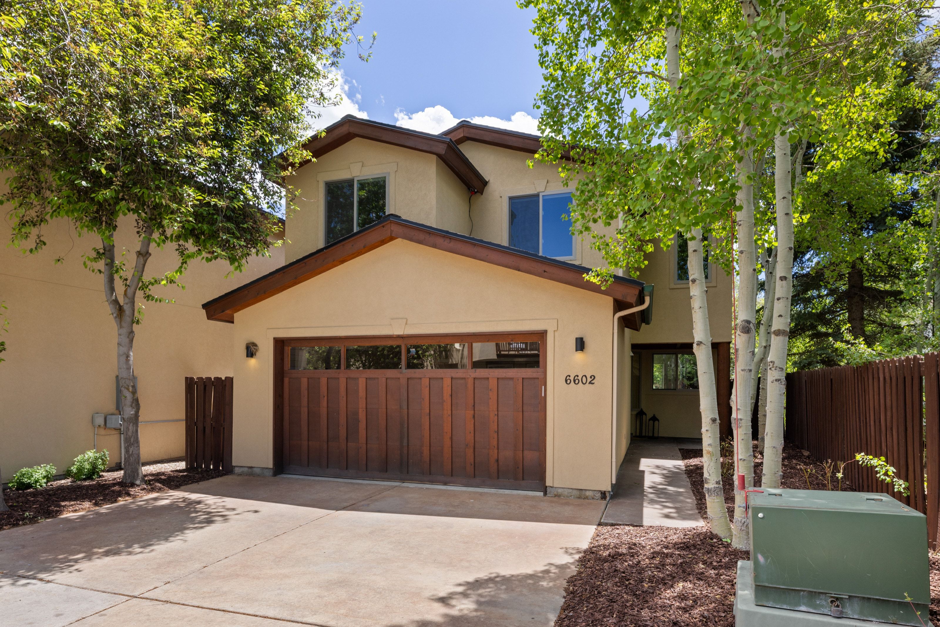Two-story stucco exterior featuring a built-in garage with a wood-panel door, concrete driveway, and mature landscaping