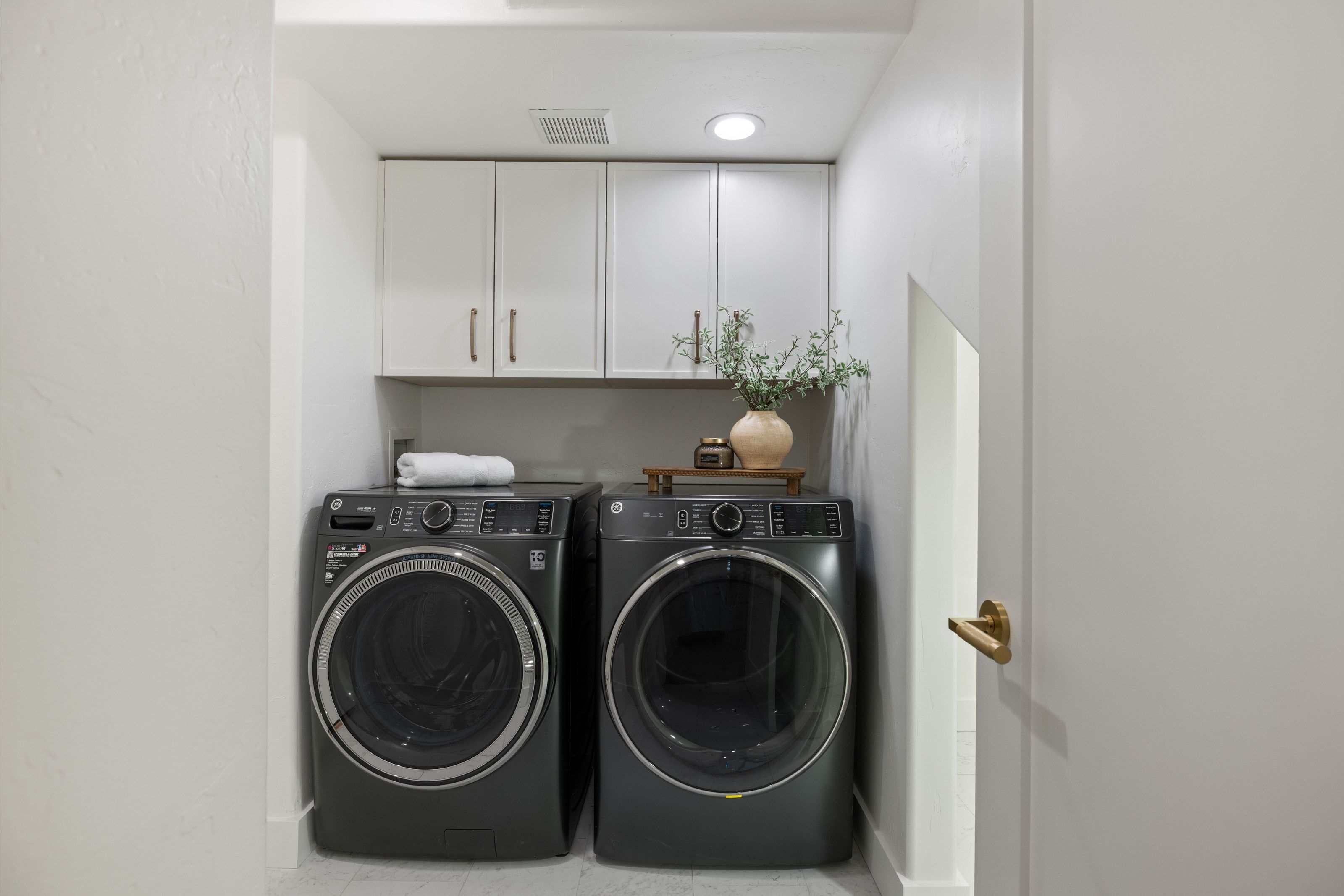 Dedicated laundry area featuring white upper cabinetry, a light-toned countertop, recessed lighting, and a gold-toned door handle