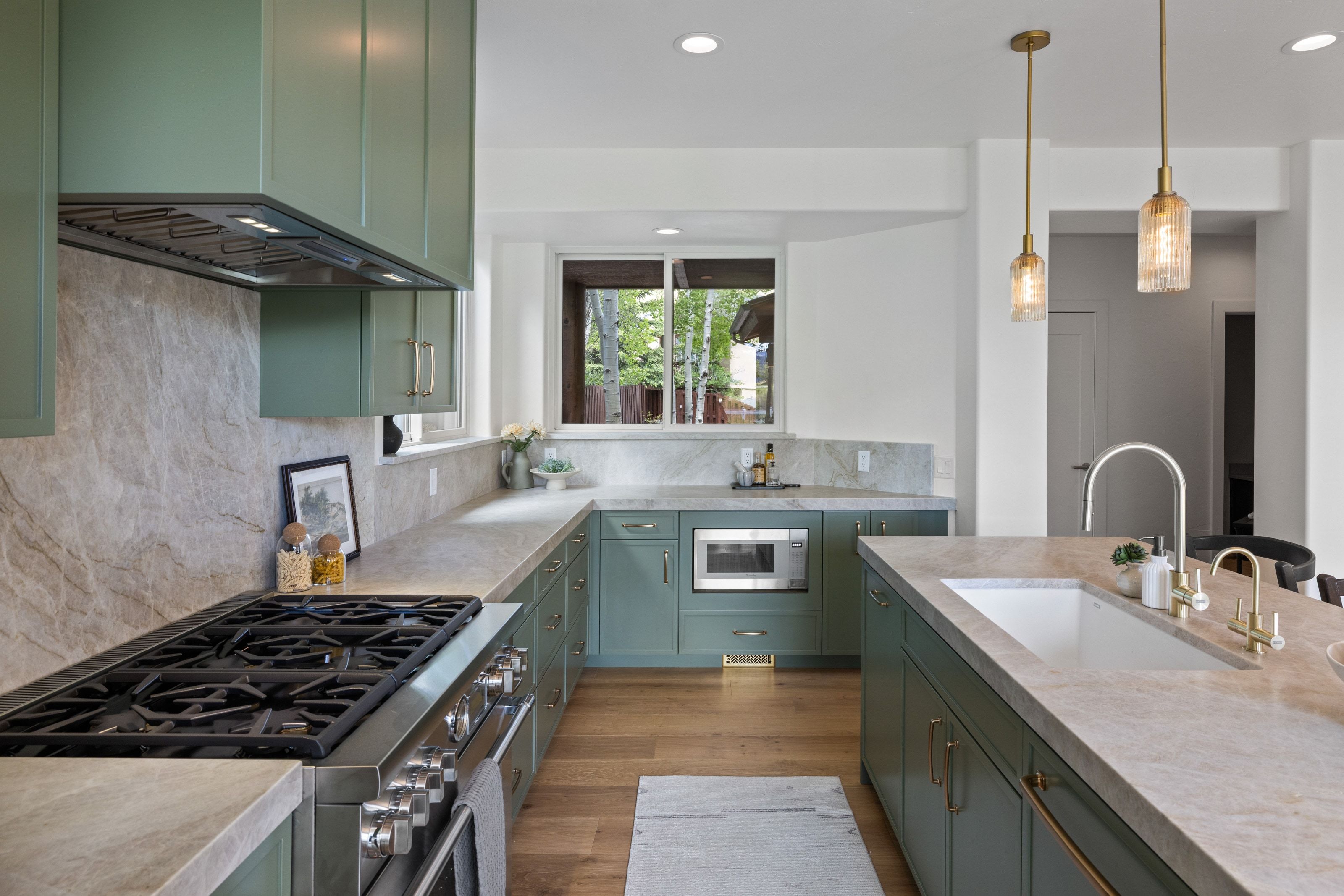 Modern kitchen featuring green cabinetry, light-toned countertops, a stainless steel range with overhead ventilation, and a built-in microwave