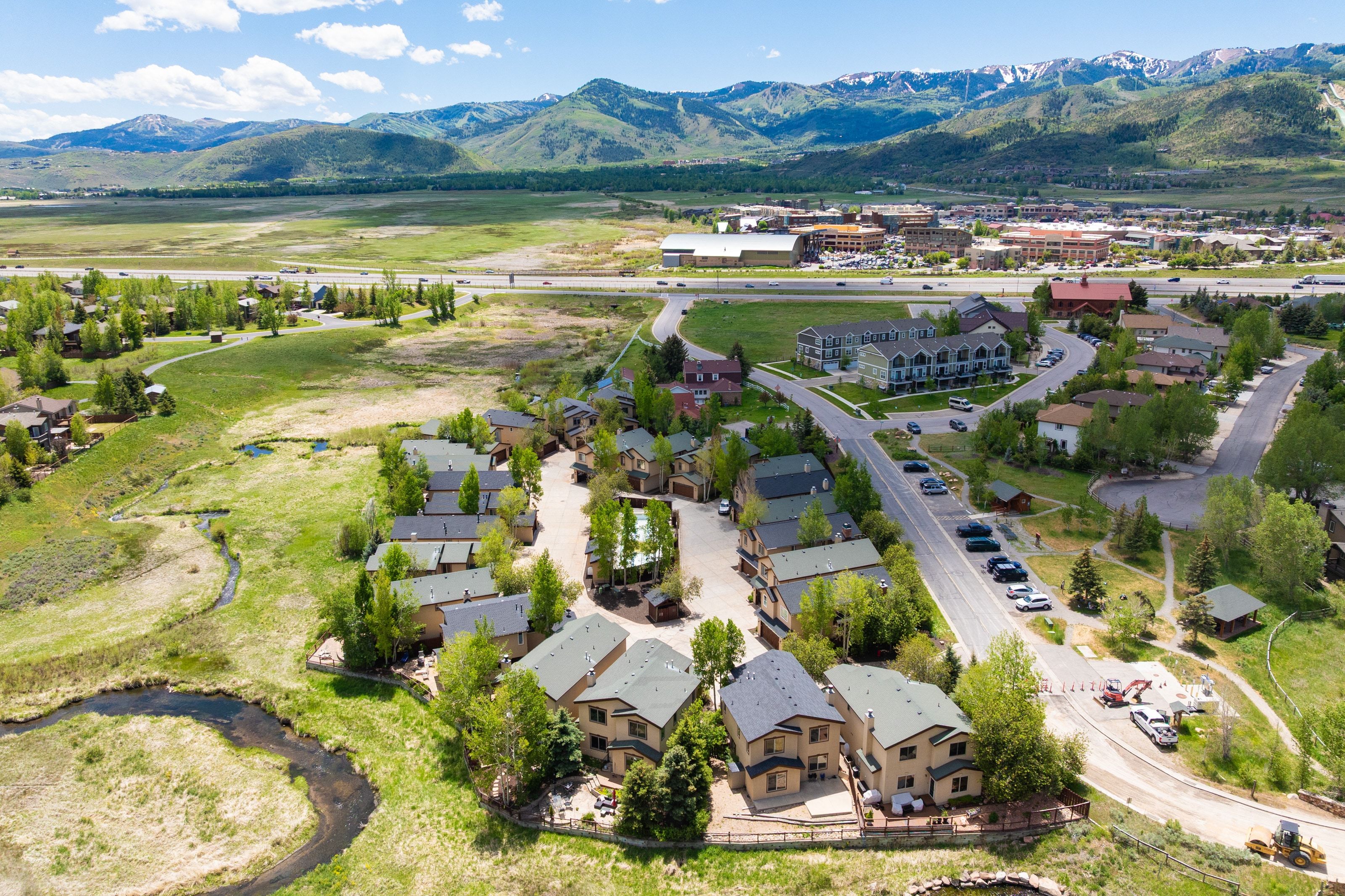 Aerial view showcasing residential properties surrounded by natural landscapes with a winding stream and distant mountains