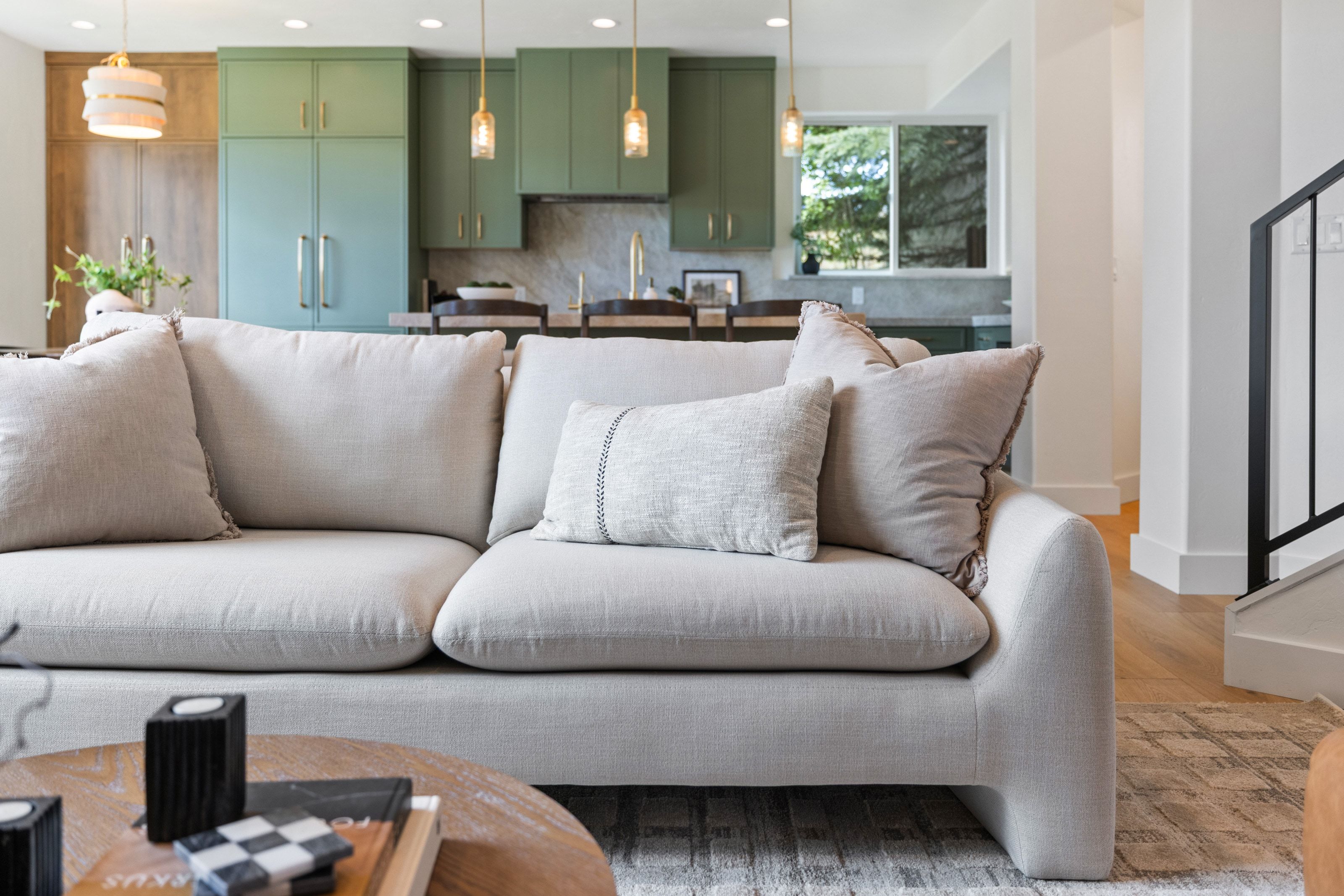 Open-concept living space featuring wood-finish flooring, a contemporary staircase with a black metal railing, and a kitchen with green cabinetry, a single window, and pendant lighting fixtures
