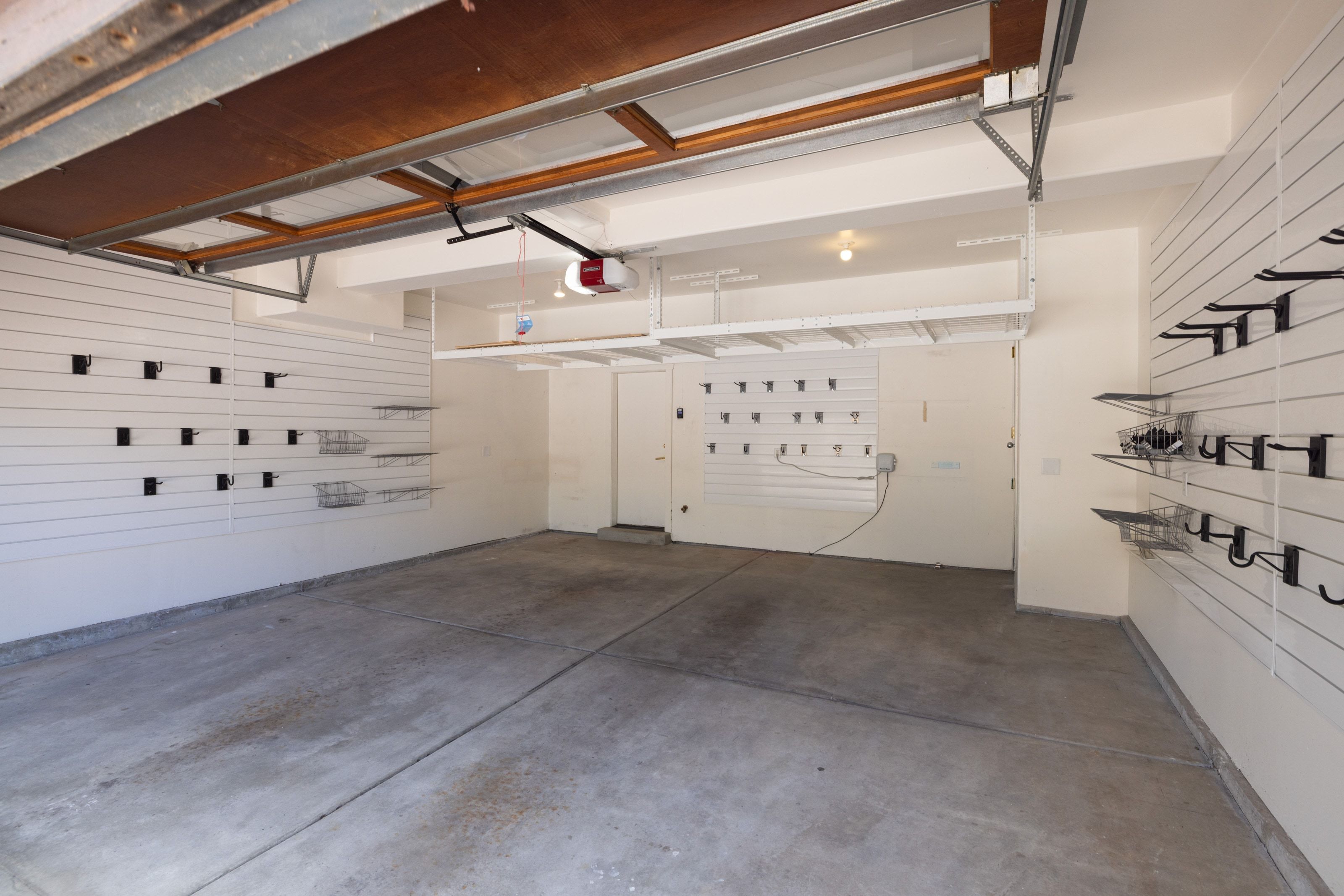 Spacious garage featuring concrete flooring, integrated slatwall storage systems with various hooks and baskets, an overhead storage rack, and a garage door opener