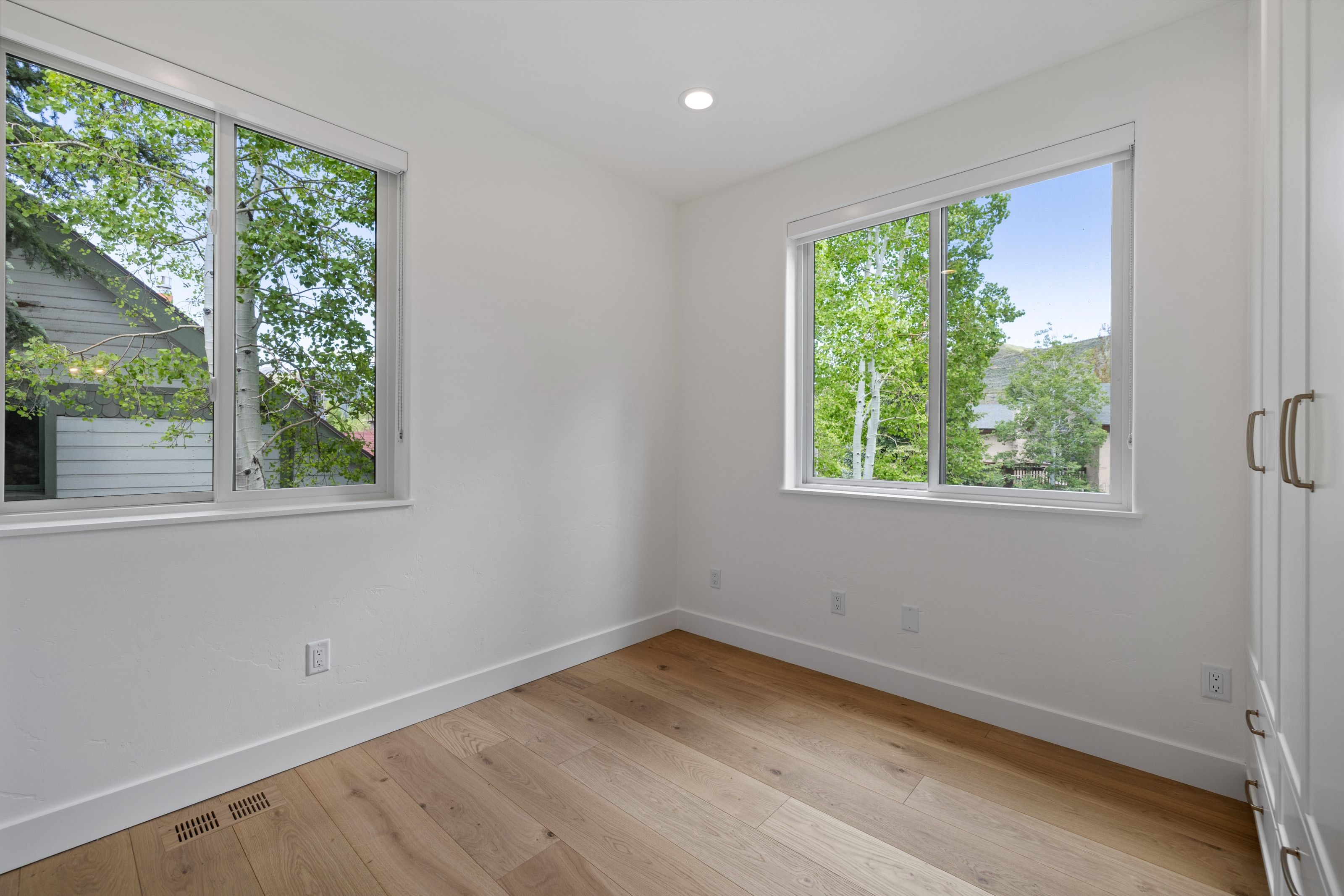 Bright room featuring two windows providing abundant natural light, wood-finish flooring, recessed lighting, and built-in white cabinetry with bronze-tone hardware
