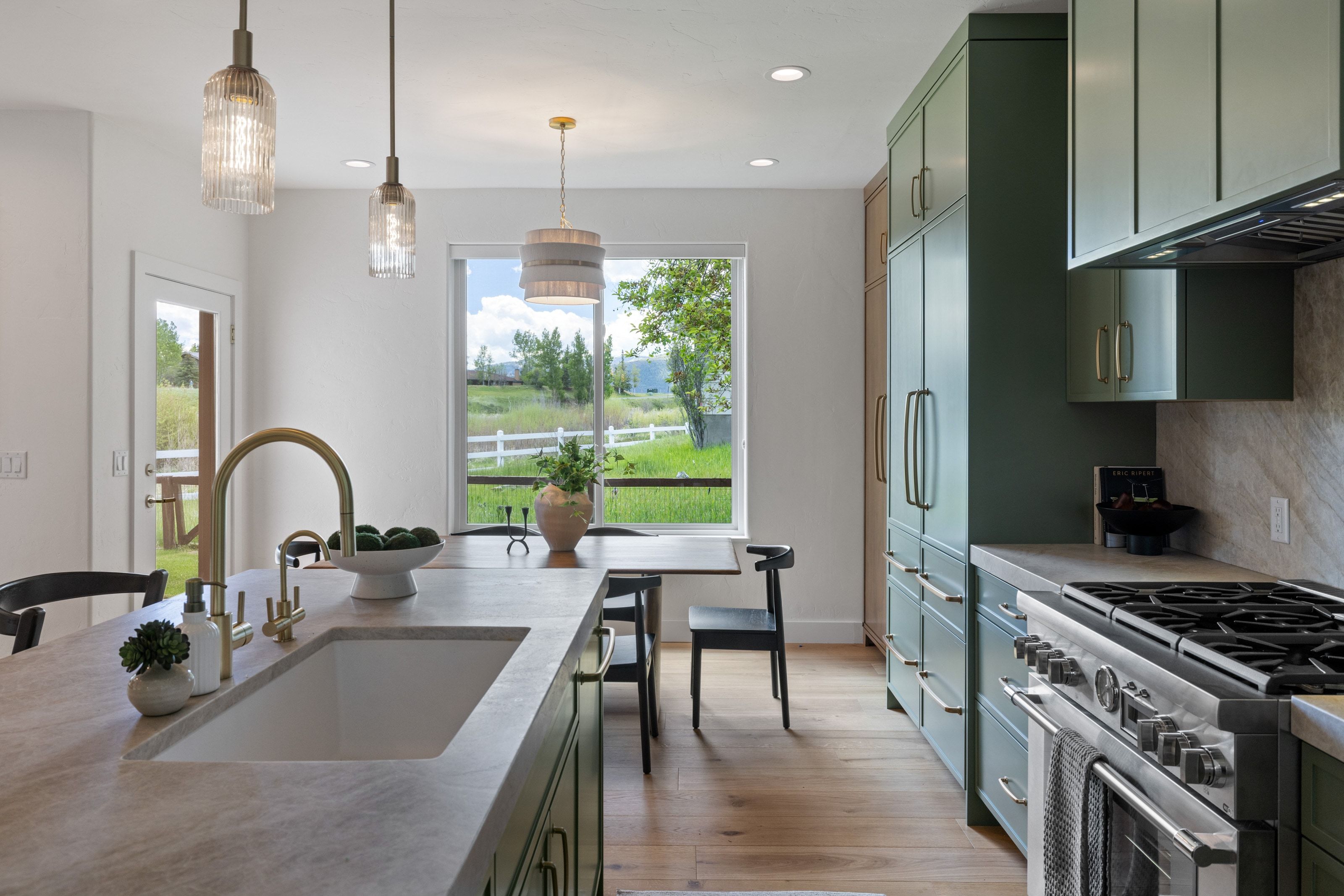 Kitchen featuring custom green cabinetry, light wood-finish flooring, a stainless steel range, a built-in sink with a gooseneck faucet, and a large window