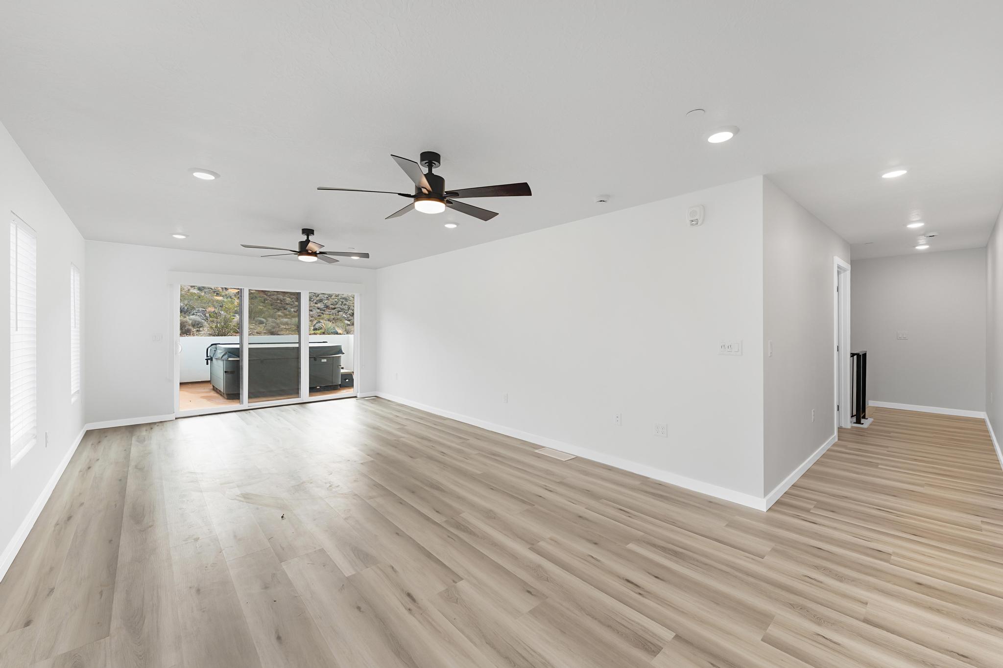 Spacious room featuring wood-finish flooring, recessed lighting, and two ceiling fans