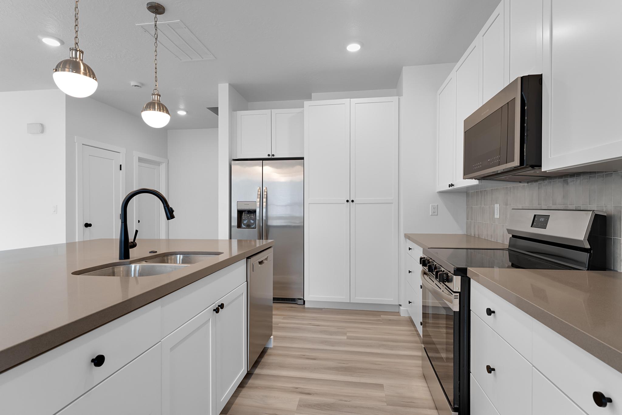 Modern kitchen featuring white shaker cabinetry, stainless steel appliances, light wood-finish flooring, a neutral-toned countertop, and an island with a double basin sink and matte black gooseneck faucet