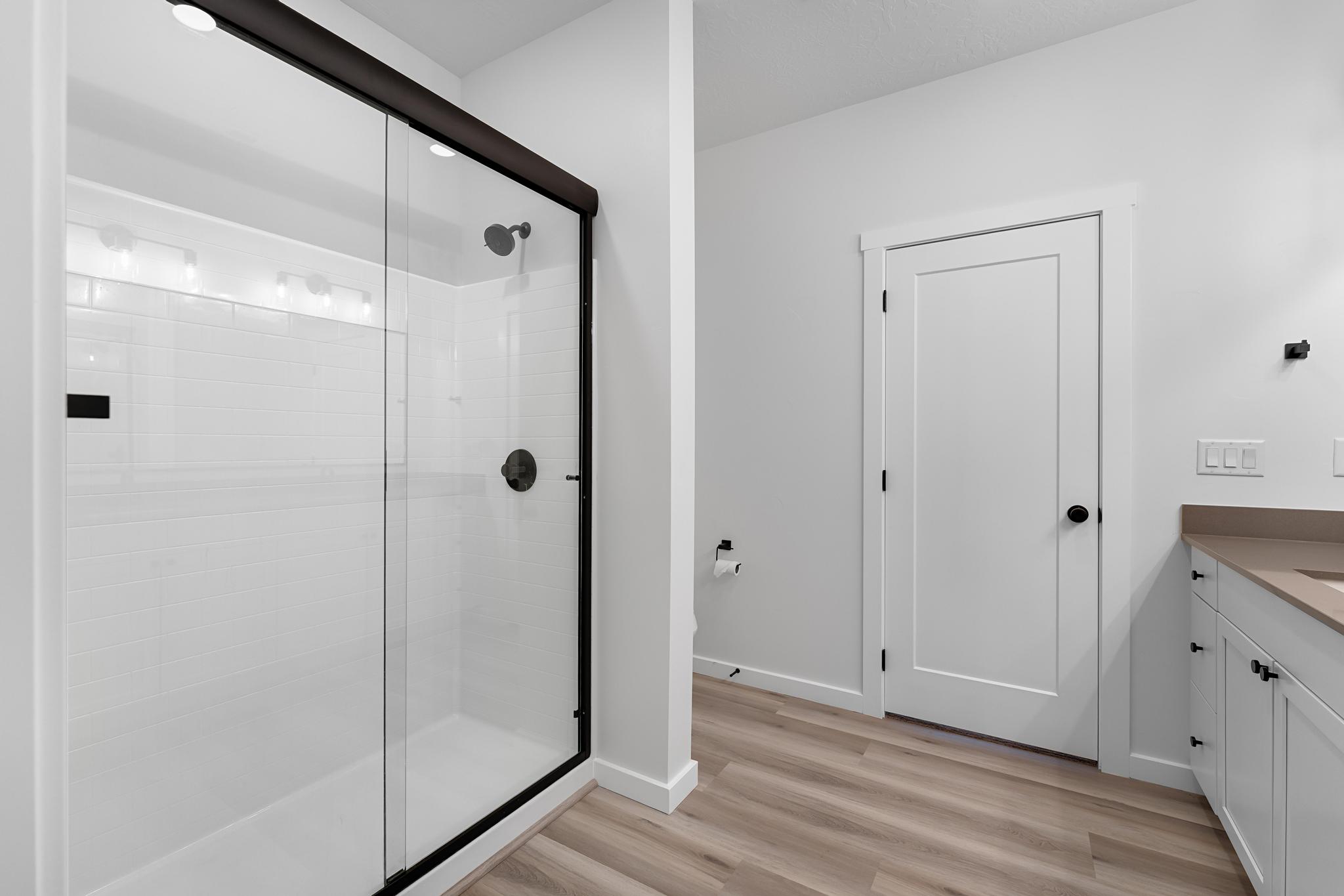Walk-in shower featuring a sliding glass door with matte black framing, white subway tile surround, and a matte black shower head