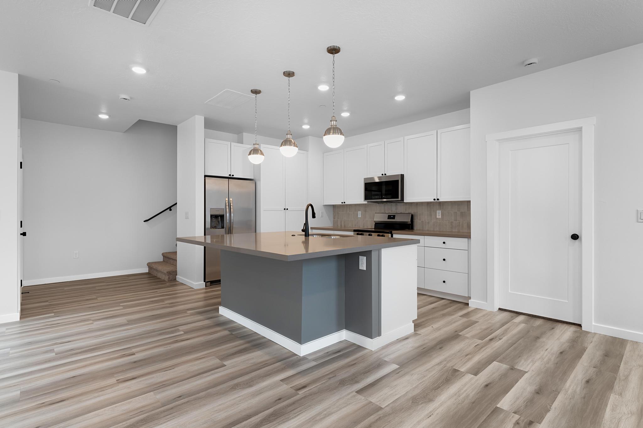 Modern kitchen featuring an expansive center island with pendant lighting, white cabinetry, integrated stainless steel appliances, and wood-finish flooring