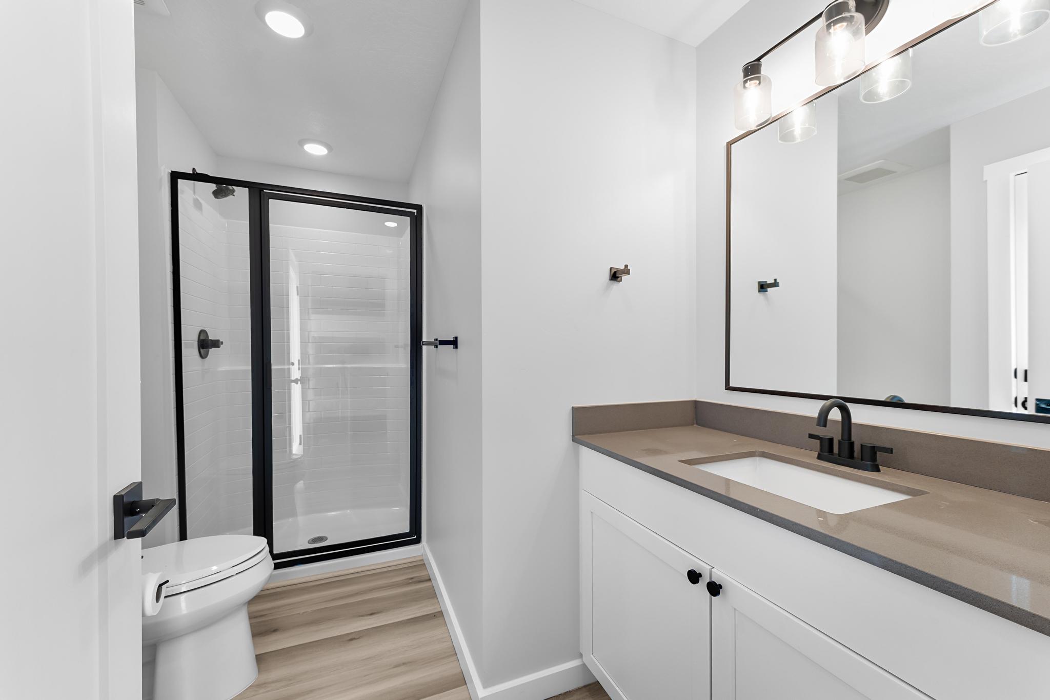Contemporary bathroom featuring a black-framed glass shower, a single vanity with a stone-finish countertop, a rectangular undermount sink, and black fixtures