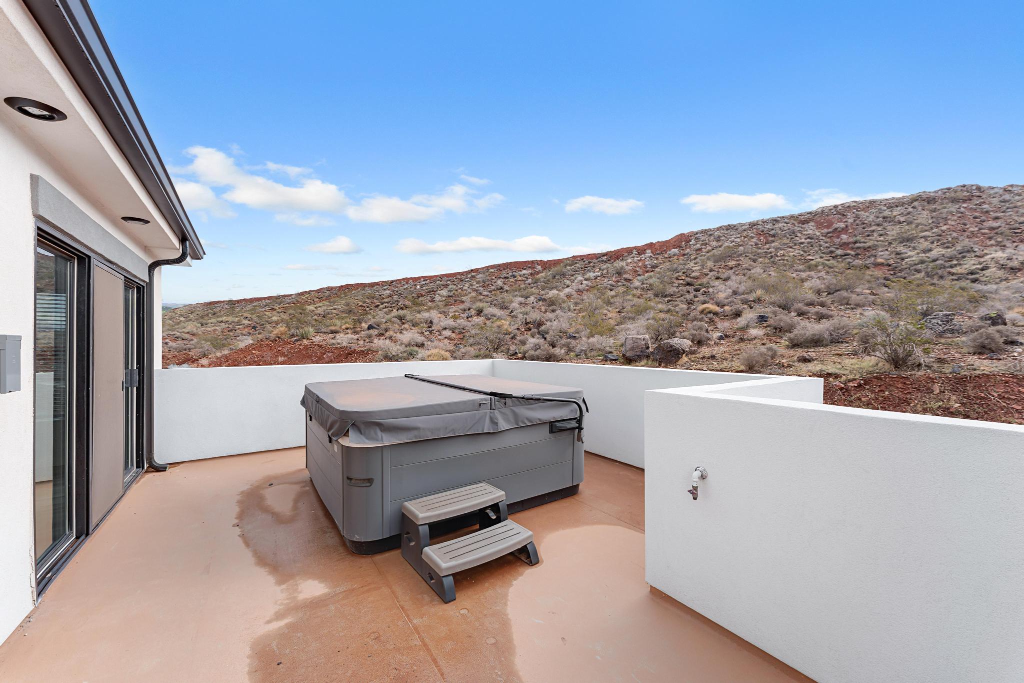 Private outdoor patio featuring a hot tub with cover, sliding glass doors, white stucco walls, and desert landscaping