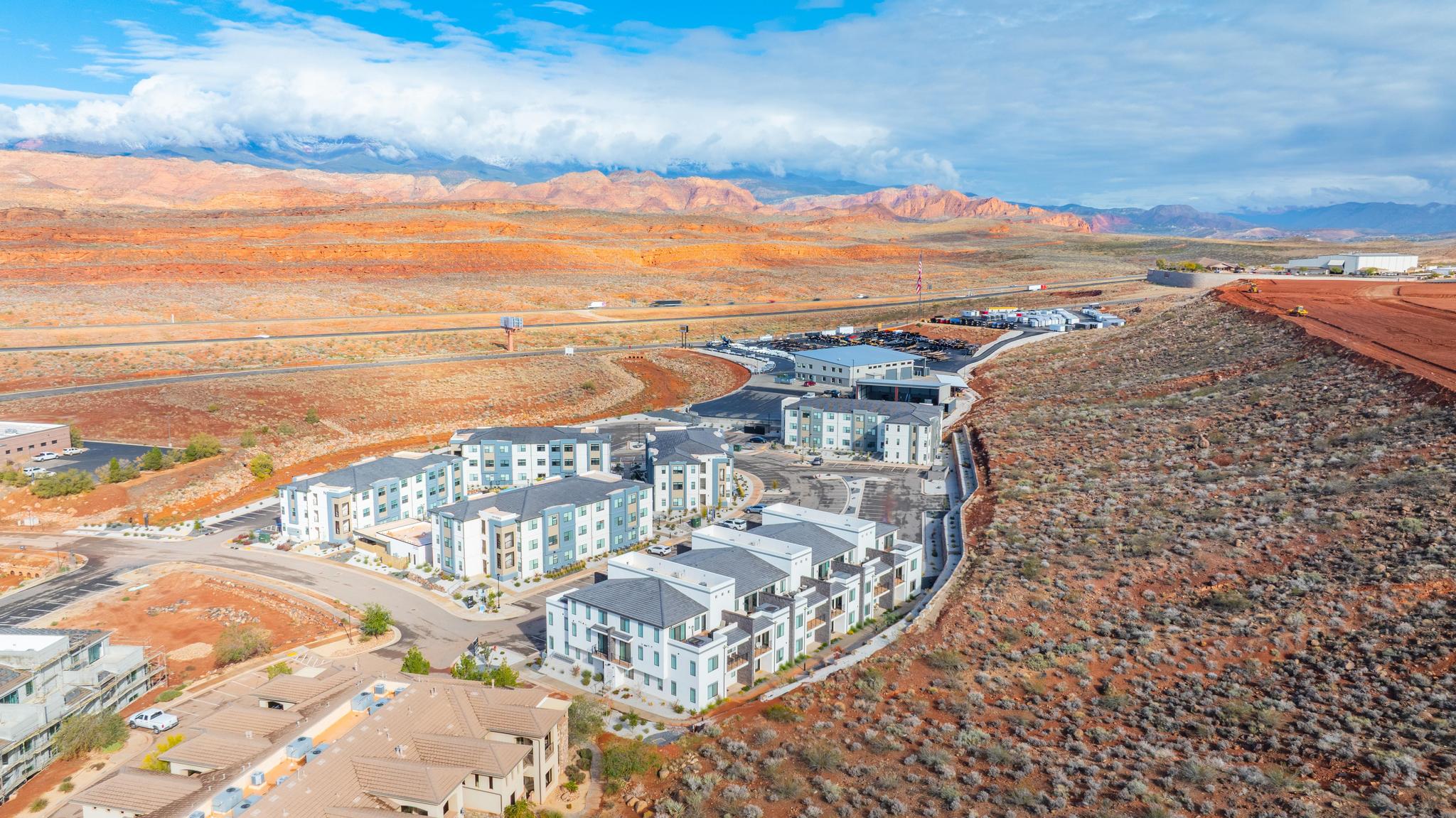Modern multi-story apartment buildings with varied exterior finishes, situated in a desert landscape with distant red rock formations
