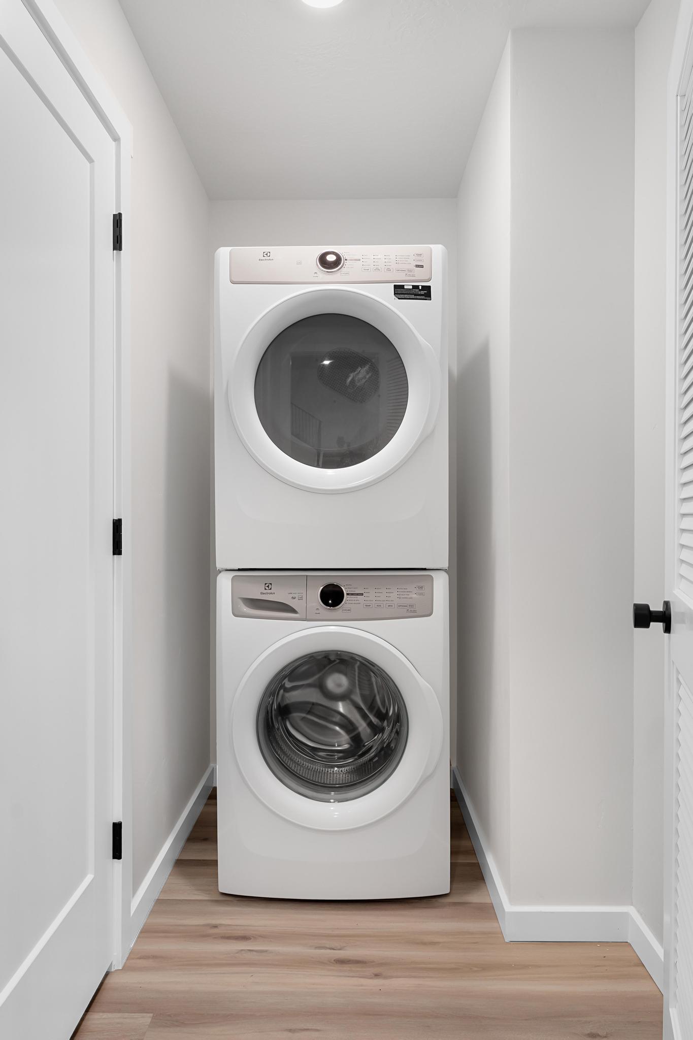 Dedicated laundry area featuring a stacked washer and dryer unit, wood-finish flooring, white baseboards, and bright recessed lighting