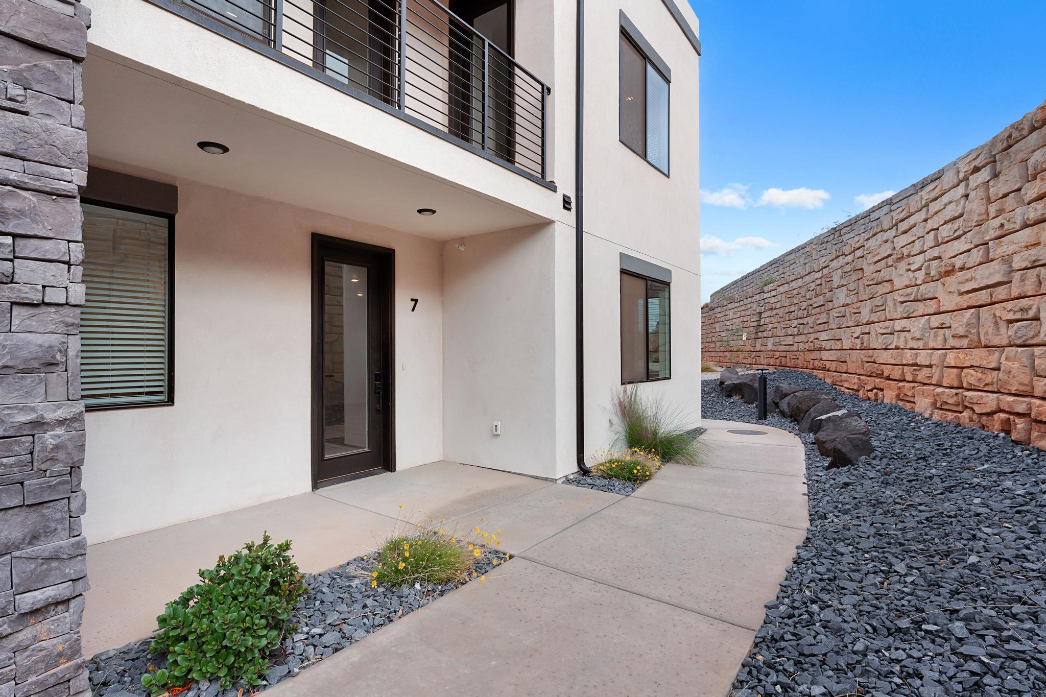 Modern exterior featuring a prominent stone veneer column, a private balcony with metal railing, and a ground-level patio