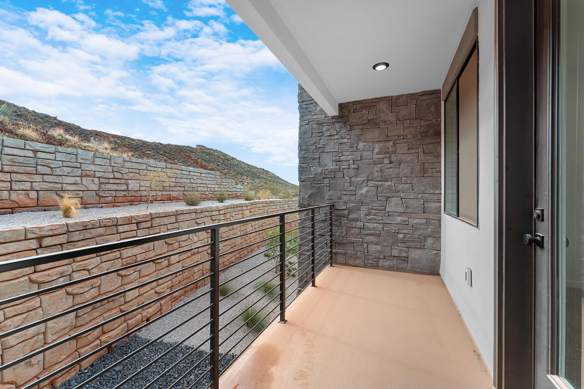 Outdoor patio featuring a modern cable railing, stone accent wall, recessed lighting, and a neutral-toned concrete floor