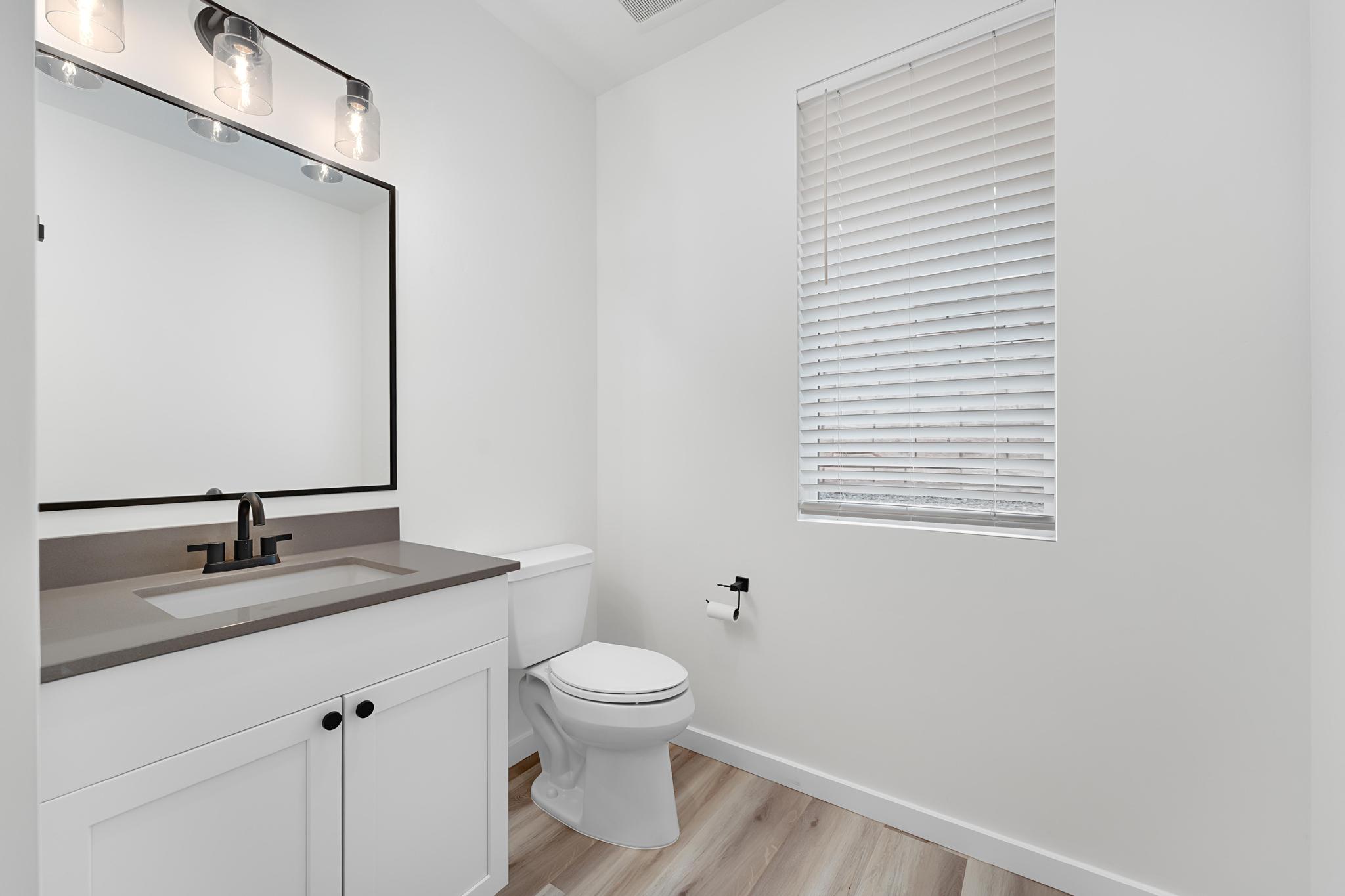 Contemporary bathroom featuring a white vanity with a gray countertop and integrated sink, matte black faucet, and a rectangular framed mirror