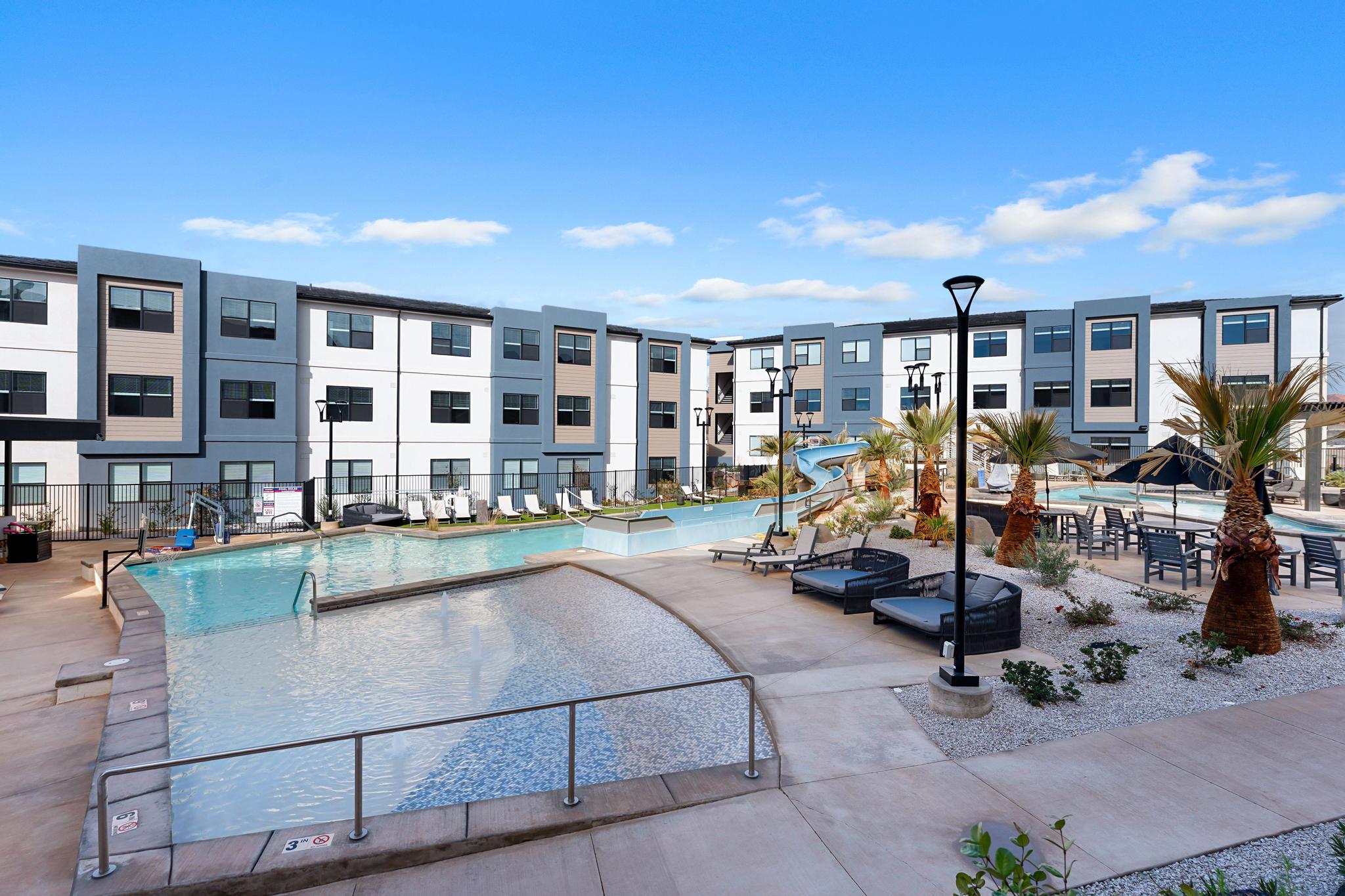 Resort-style pool area featuring a large swimming pool, integrated water slide, and surrounding concrete decking