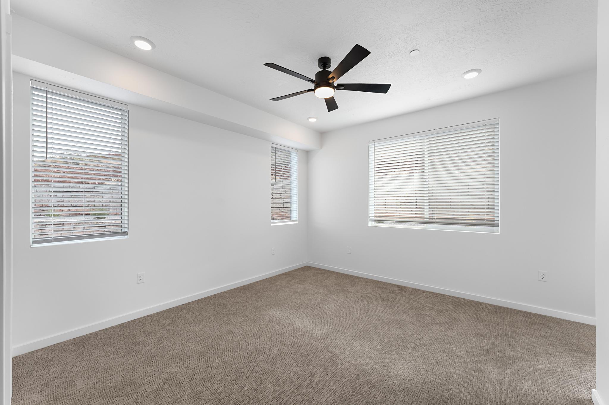 Spacious room featuring textured carpeting, white walls, and multiple windows with horizontal blinds