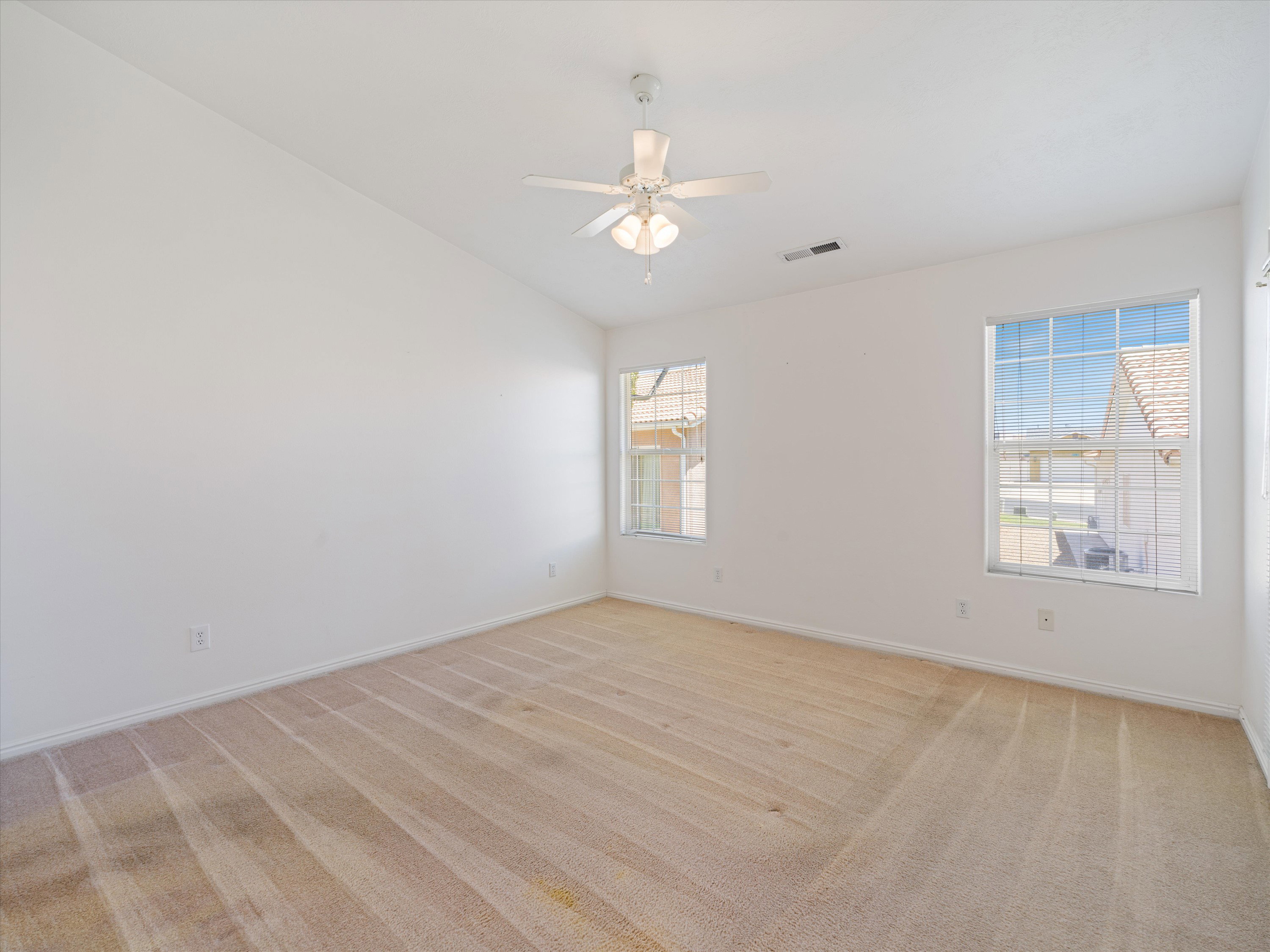 Vaulted ceiling room with two windows, ceiling fan, and neutral carpeting