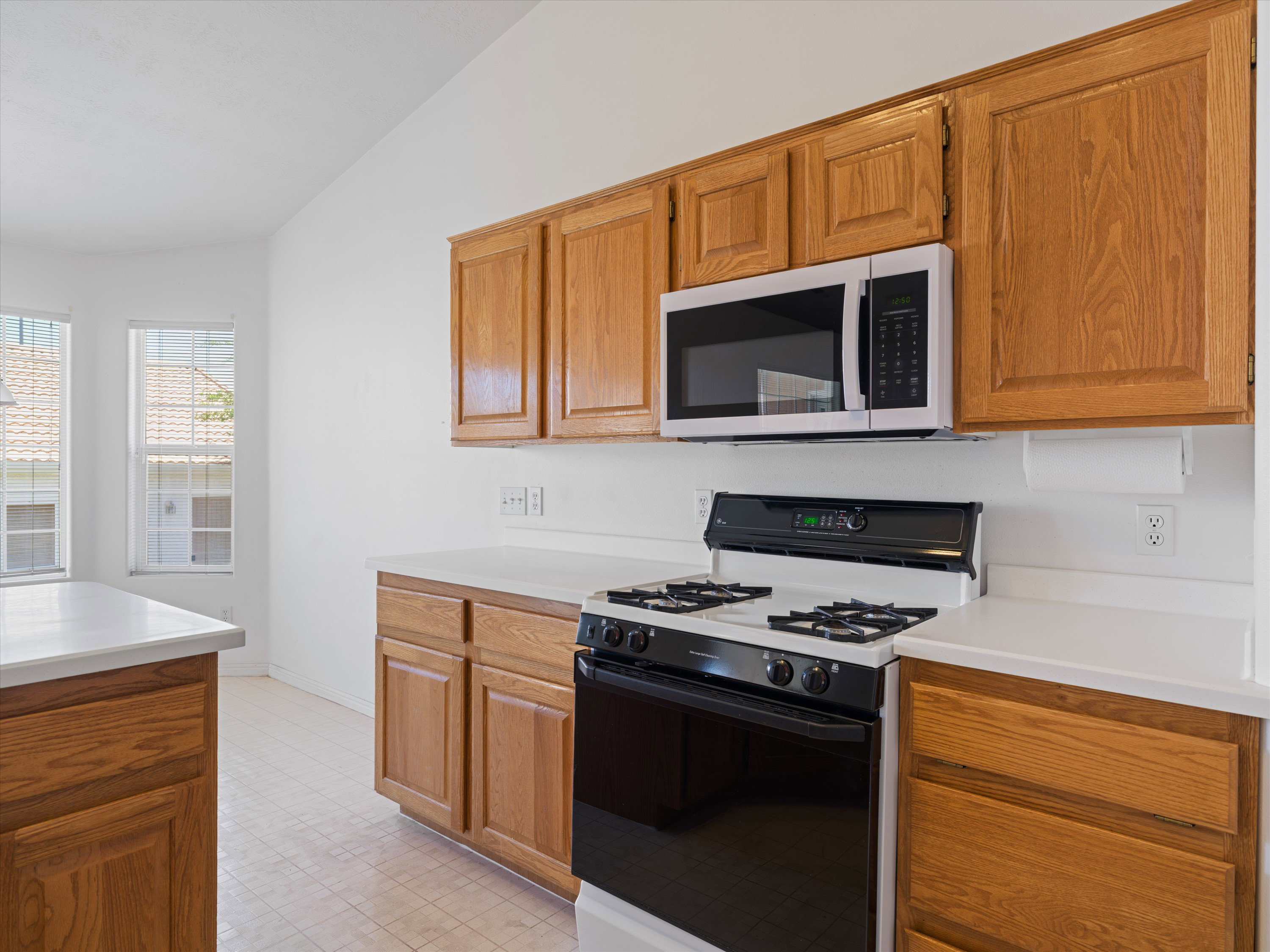 Kitchen featuring wood cabinetry, white countertops, a built-in microwave, a black and white range, and tiled flooring