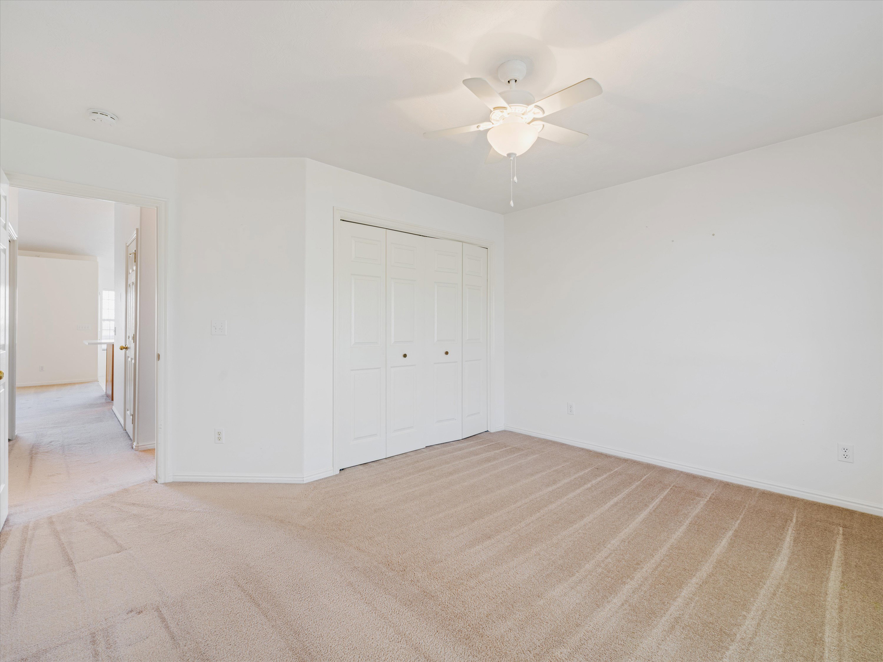 Carpeted room featuring a ceiling fan with integrated lighting, white walls, and bi-fold closet doors