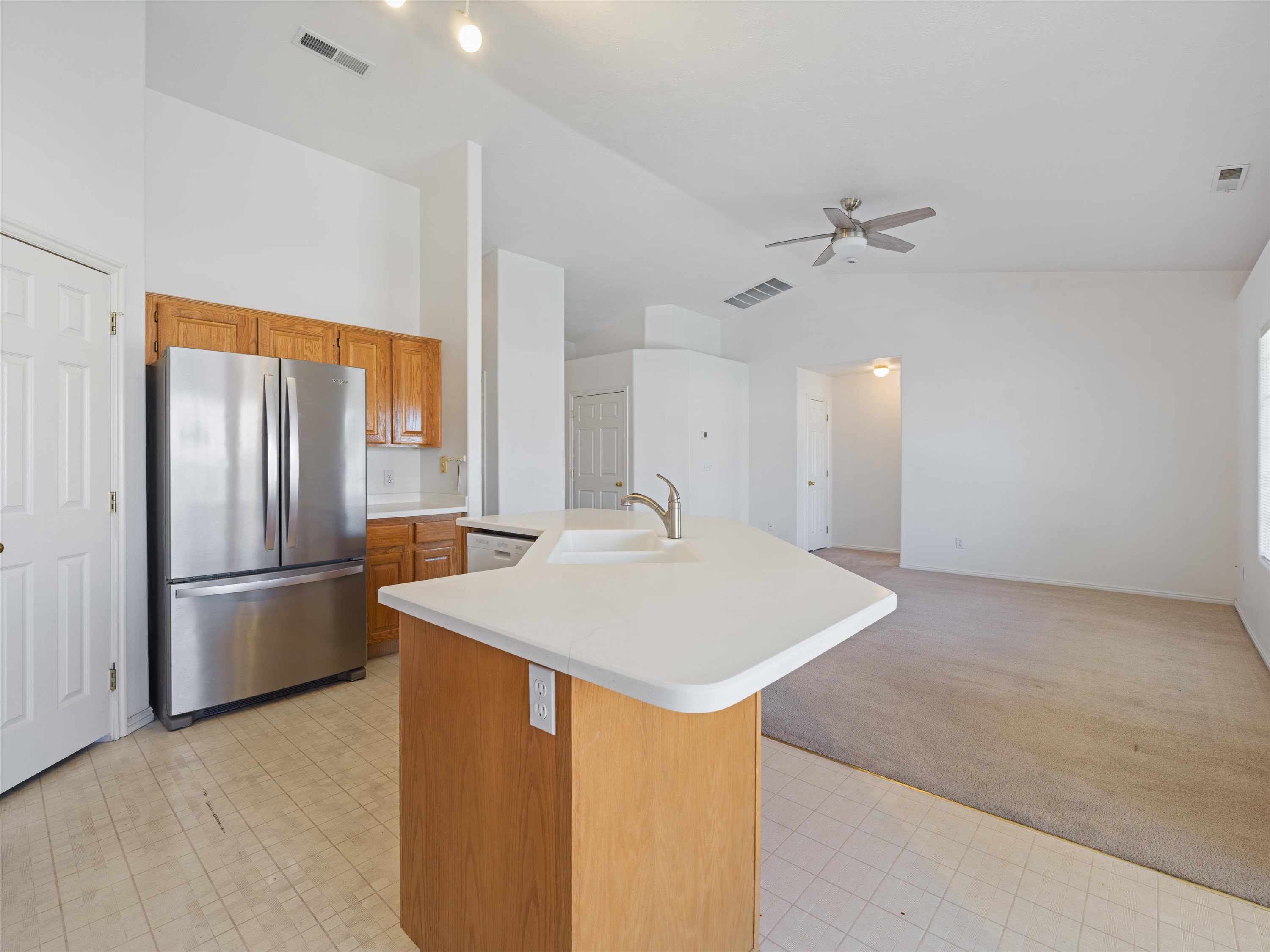 Kitchen featuring wood cabinetry, white countertops, a stainless steel refrigerator, and a kitchen island with an integrated sink