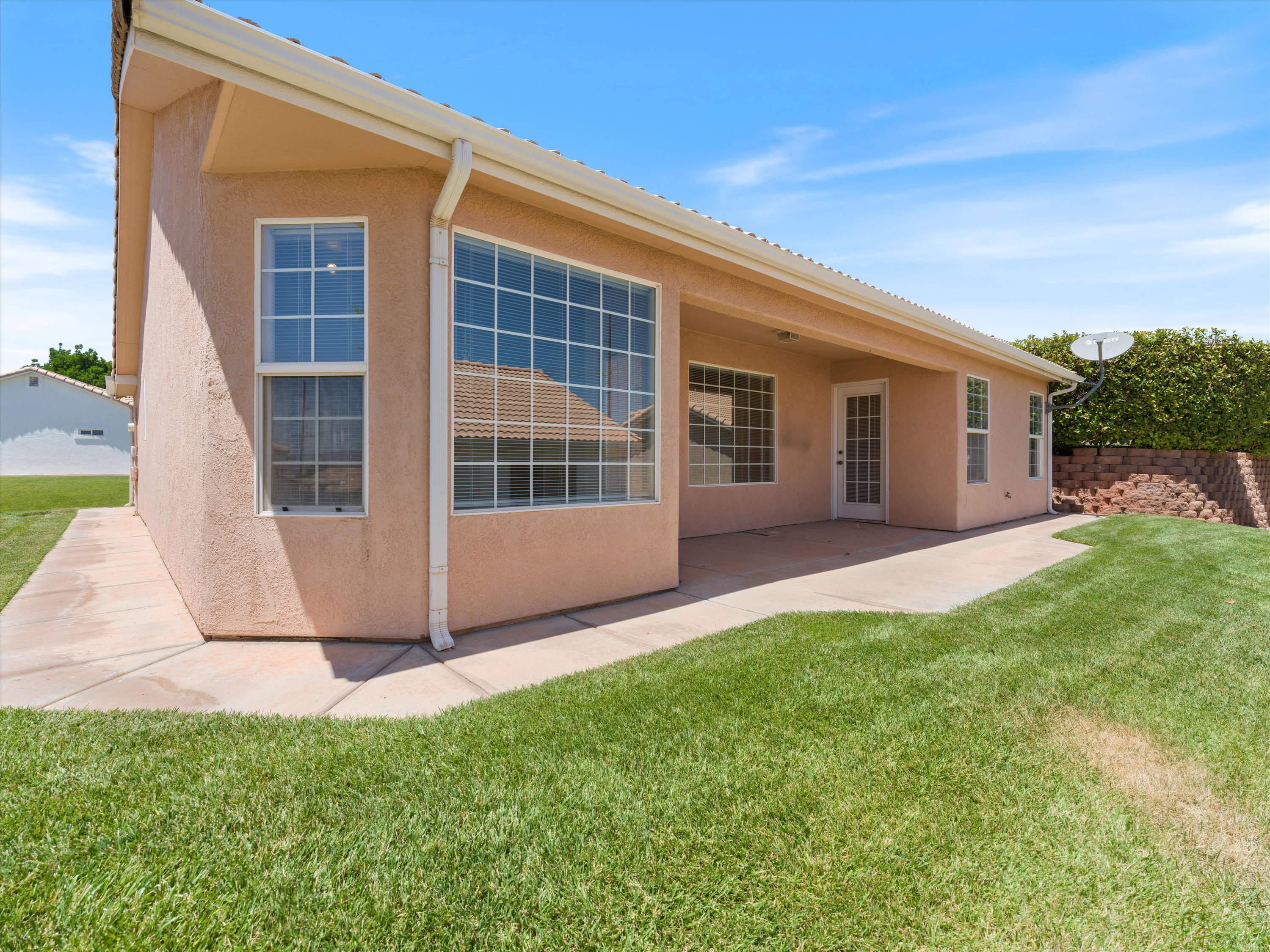 Rear exterior featuring stucco finish, expansive windows with grid patterns, a covered patio area, and a lush green lawn