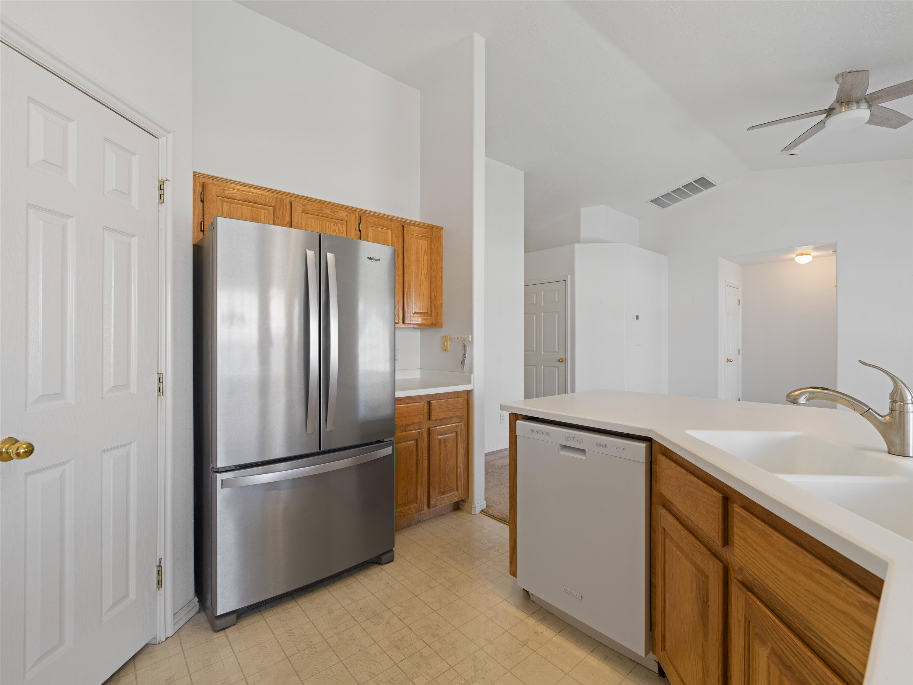 Kitchen featuring wood cabinetry, stainless steel refrigerator, white dishwasher, and a double basin sink with a gooseneck faucet