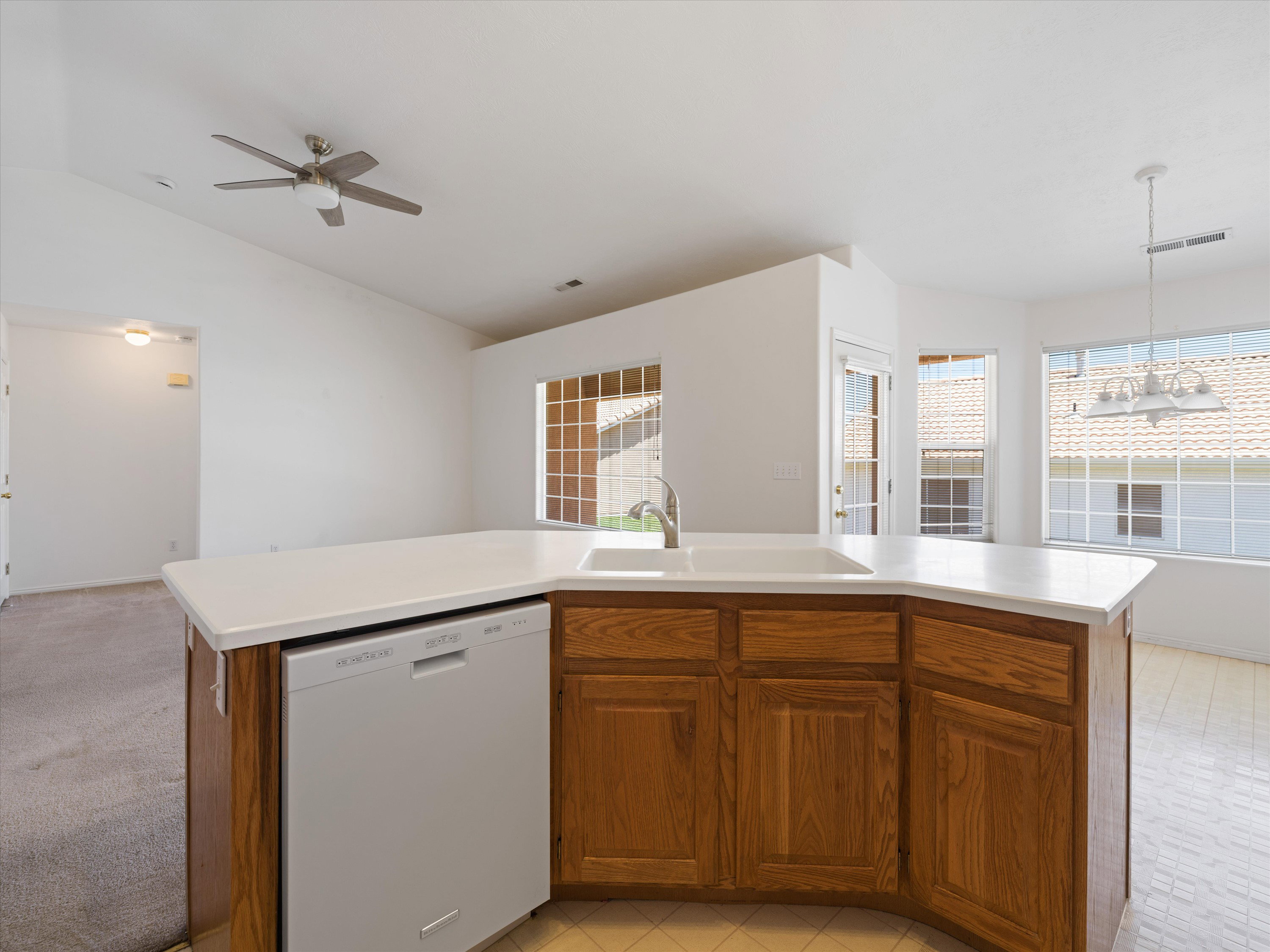 Peninsula kitchen island with a white countertop and integrated sink, featuring wood-finish cabinetry and a built-in dishwasher
