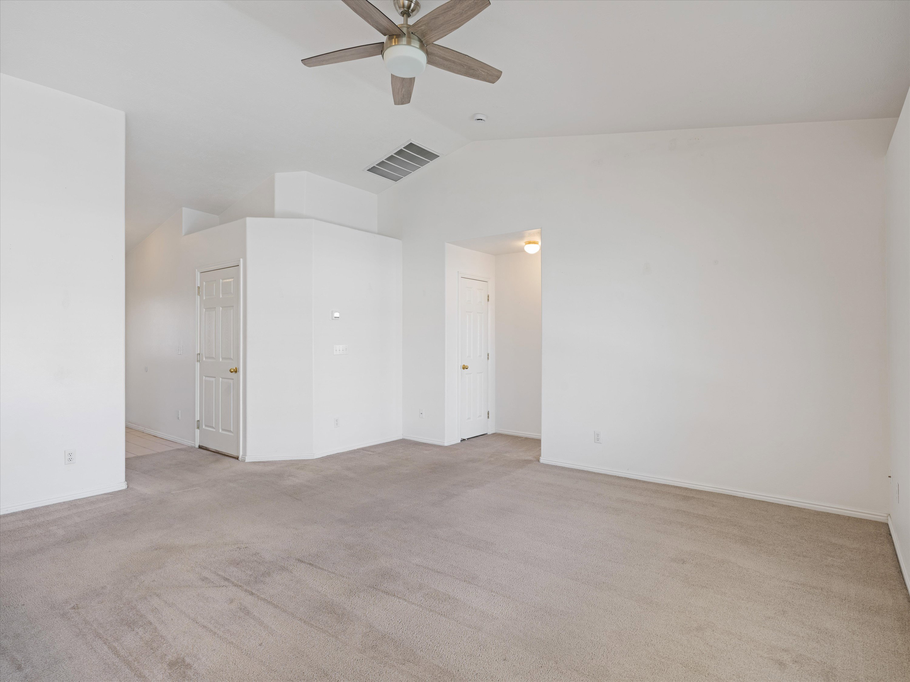 Spacious room featuring vaulted ceilings, light-colored carpeting, a ceiling fan with integrated lighting, and multiple interior doors