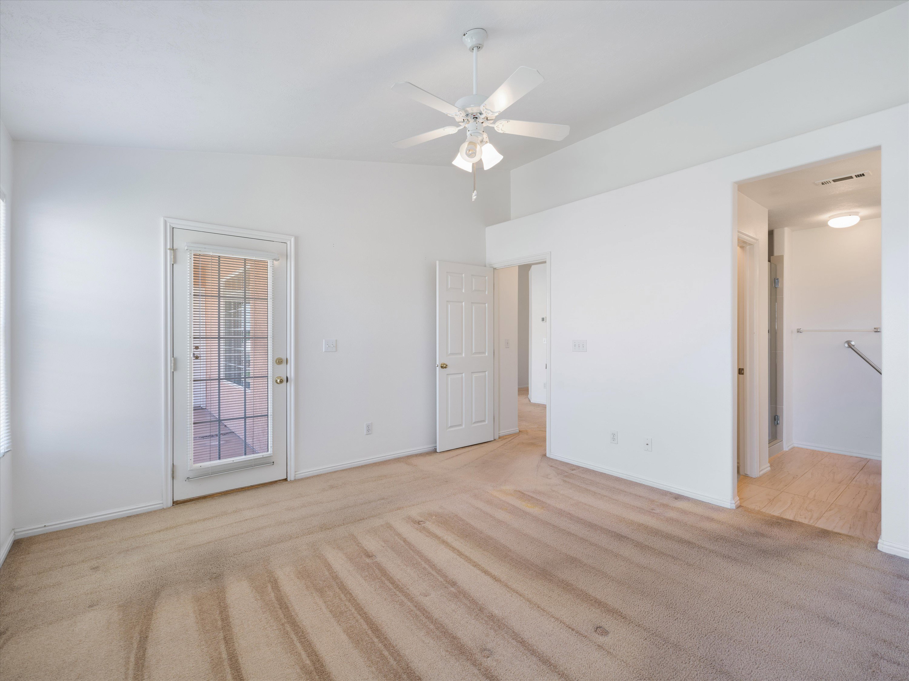 Carpeted room featuring a white ceiling fan with light fixture, a glass-paned door, and white painted walls