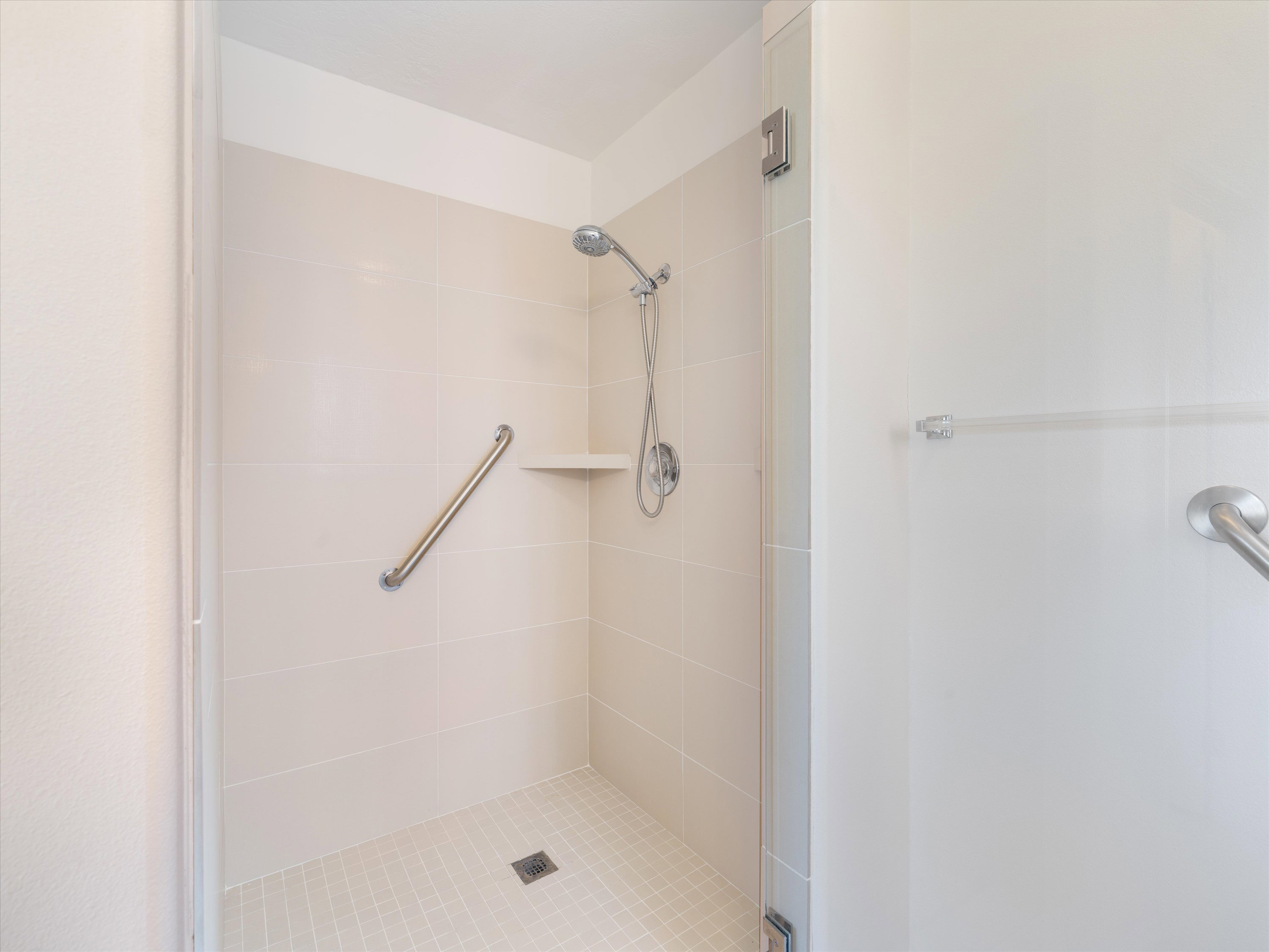 Shower enclosure featuring light-colored wall tiles, a built-in corner shelf, and a handheld showerhead