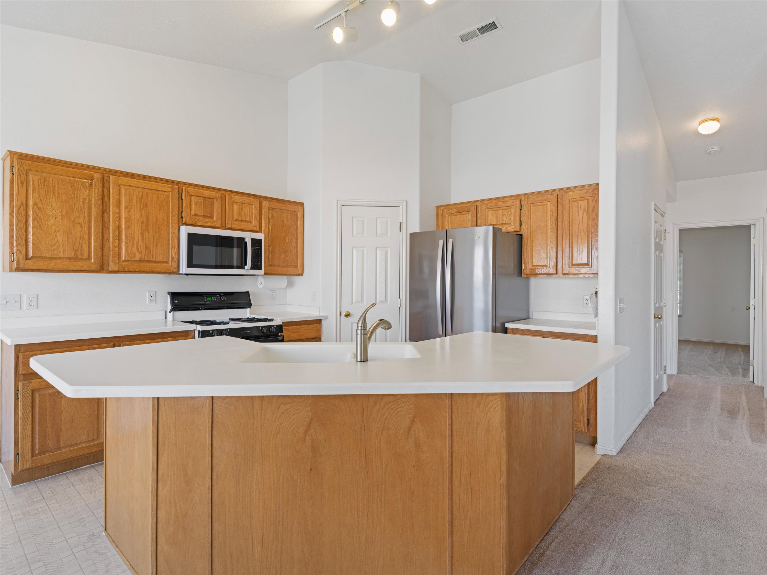 Kitchen featuring a central island with a solid surface countertop, wood cabinetry, stainless steel appliances, and track lighting