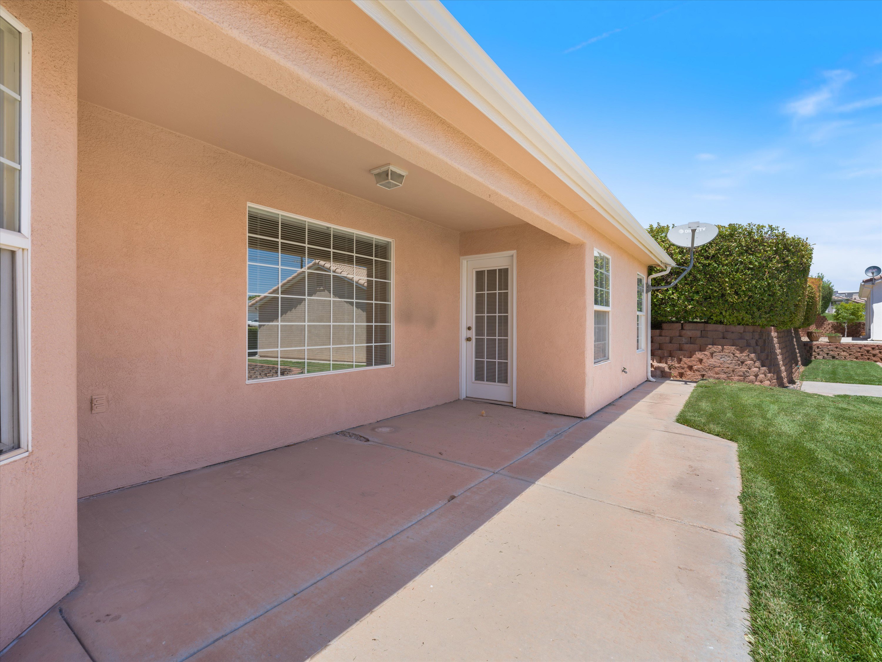 Covered concrete patio with stucco exterior, multiple windows, and direct access door
