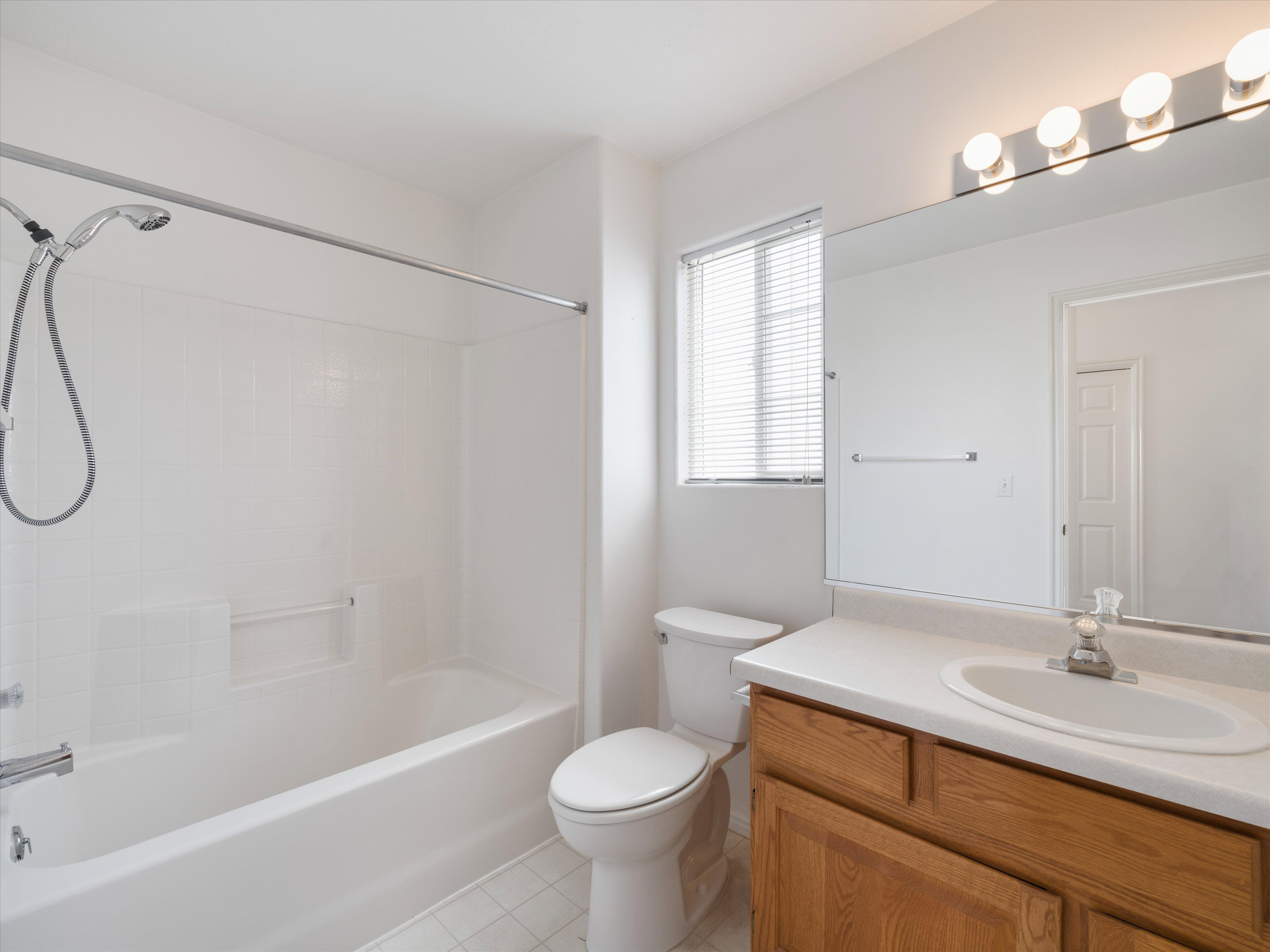 Bathroom featuring a white tub/shower combination with tiled surround, a toilet, and a vanity with a wood-finish cabinet and integrated sink