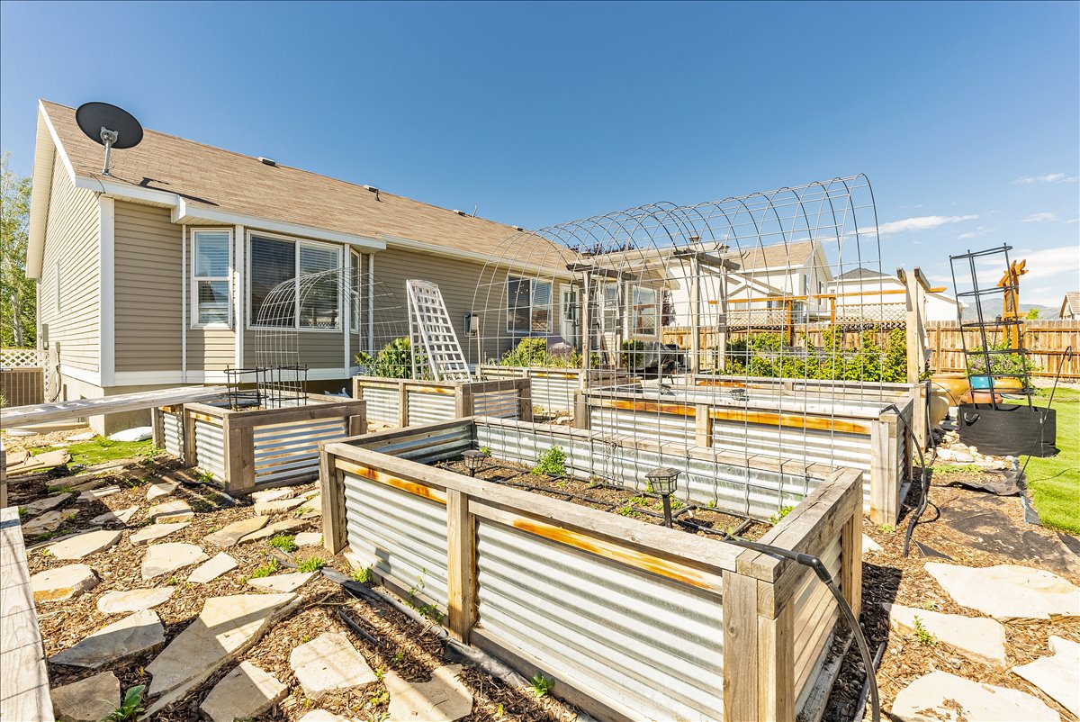 Rear exterior featuring multiple raised garden beds with corrugated metal siding and wood framing, stone pathway, and a well-maintained lawn area