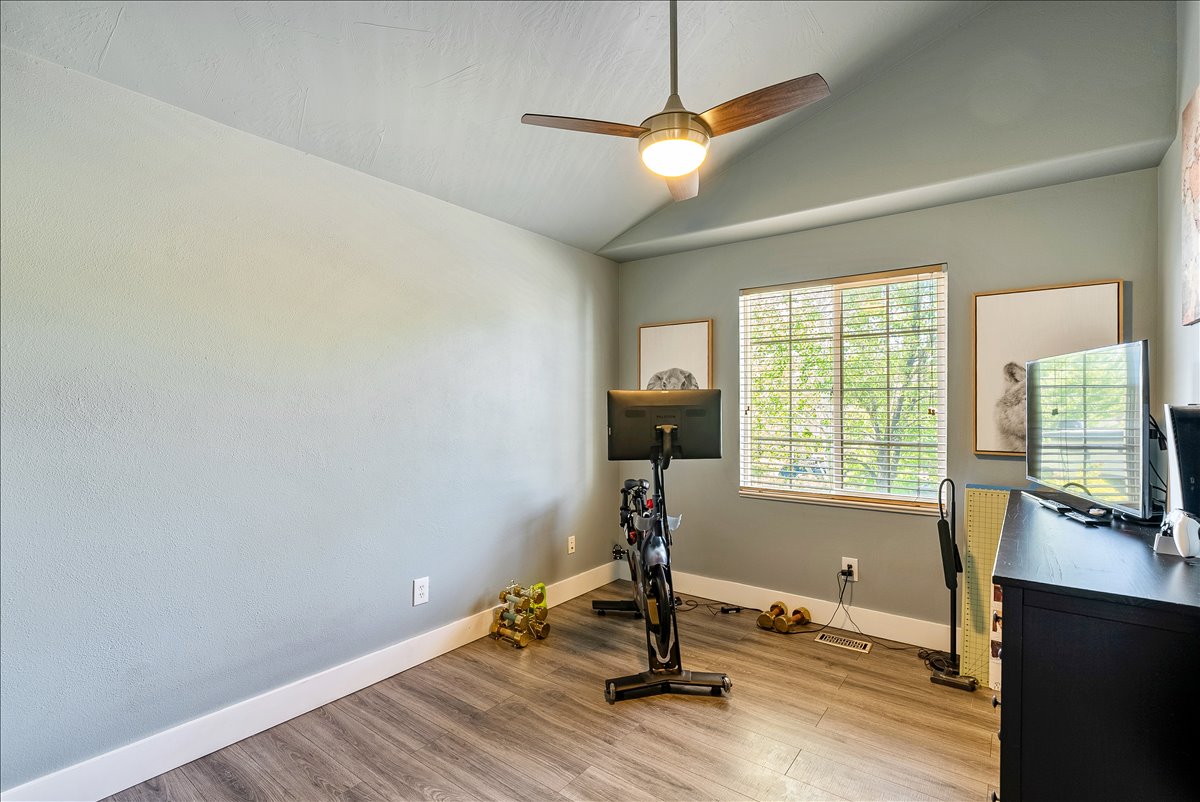Vaulted ceiling room featuring wood-finish flooring and a window with horizontal blinds