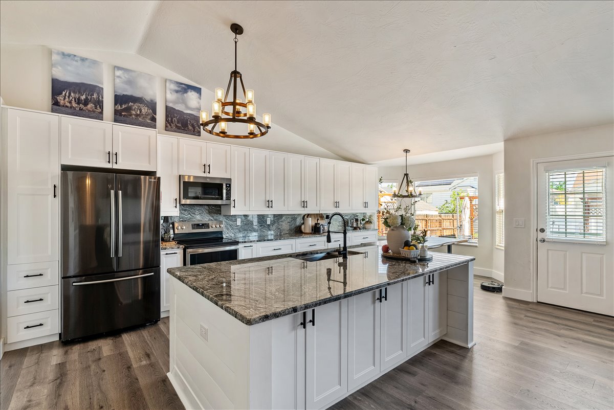 Open-concept kitchen featuring white cabinetry, dark wood-finish flooring, a central island with a stone countertop, stainless steel appliances, and a vaulted ceiling with decorative lighting