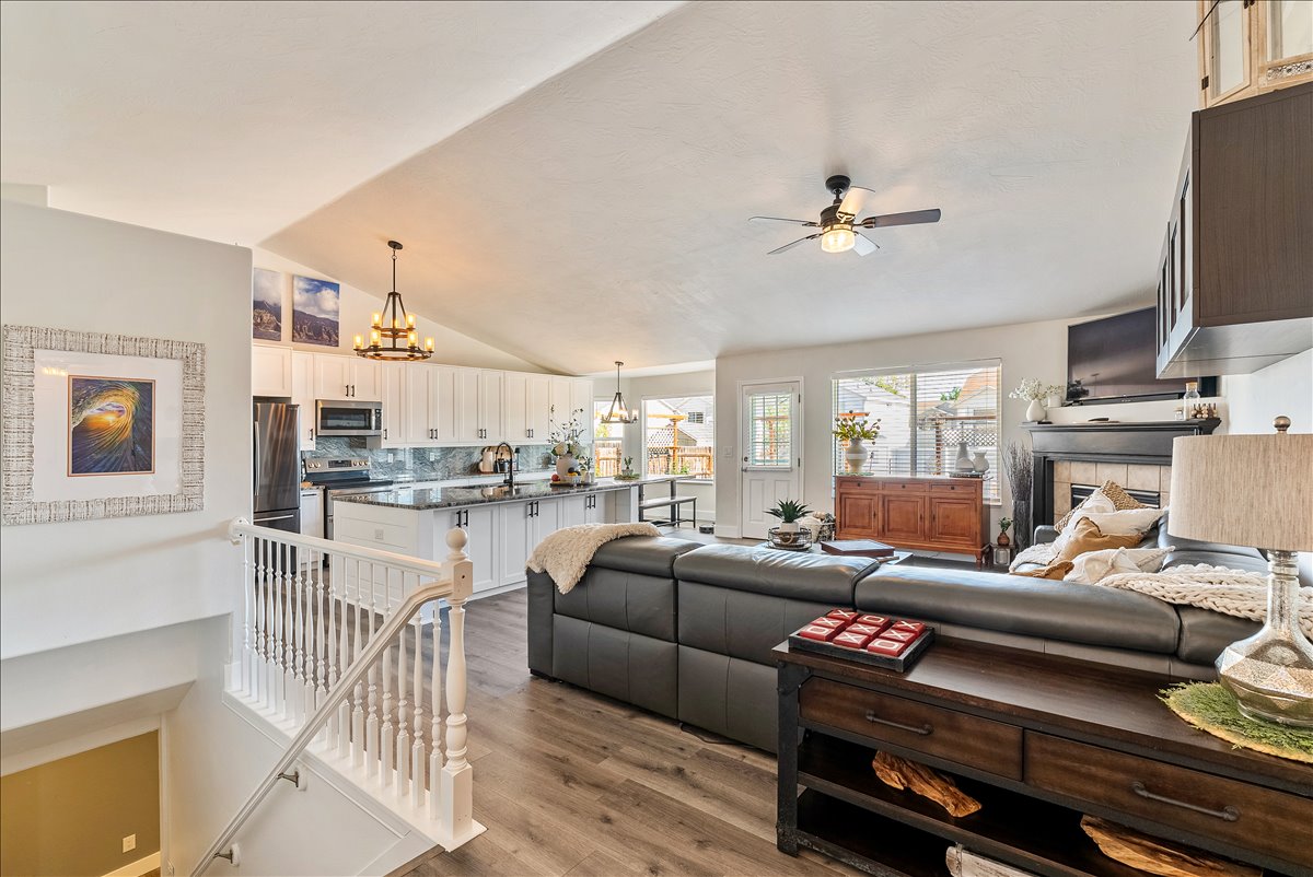 Open-concept living space featuring vaulted ceilings, wood-finish flooring, and a contemporary kitchen with white cabinetry and dark countertops