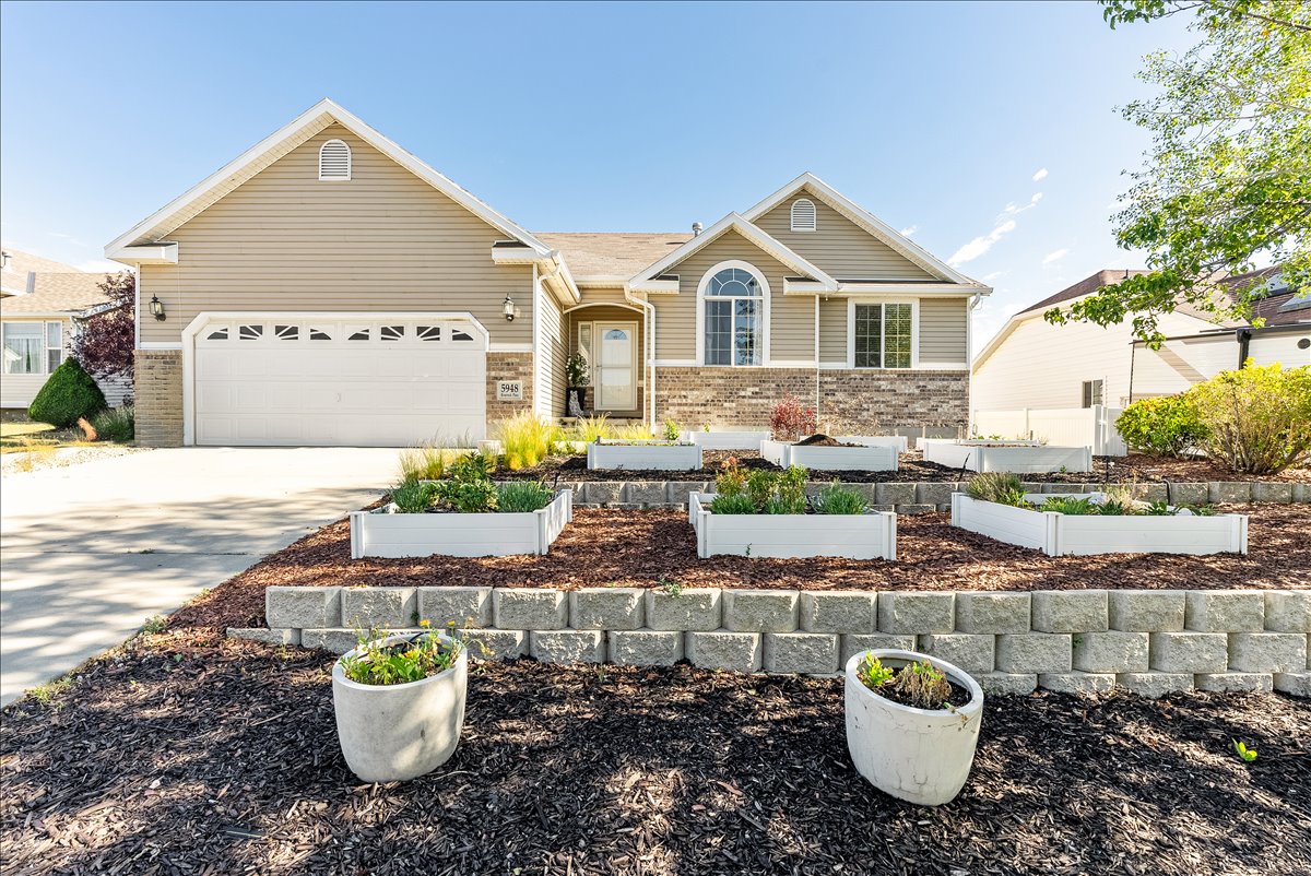 Inviting residential exterior featuring a two-car garage, stone facade accents, arched window, and a tiered front yard with raised garden beds and retaining walls