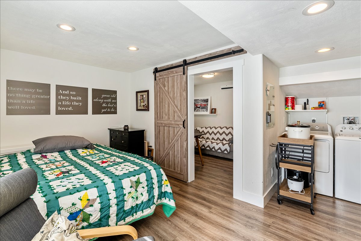 Bedroom space featuring wood-finish flooring, recessed lighting, a sliding barn door, and a dedicated laundry area with built-in shelving